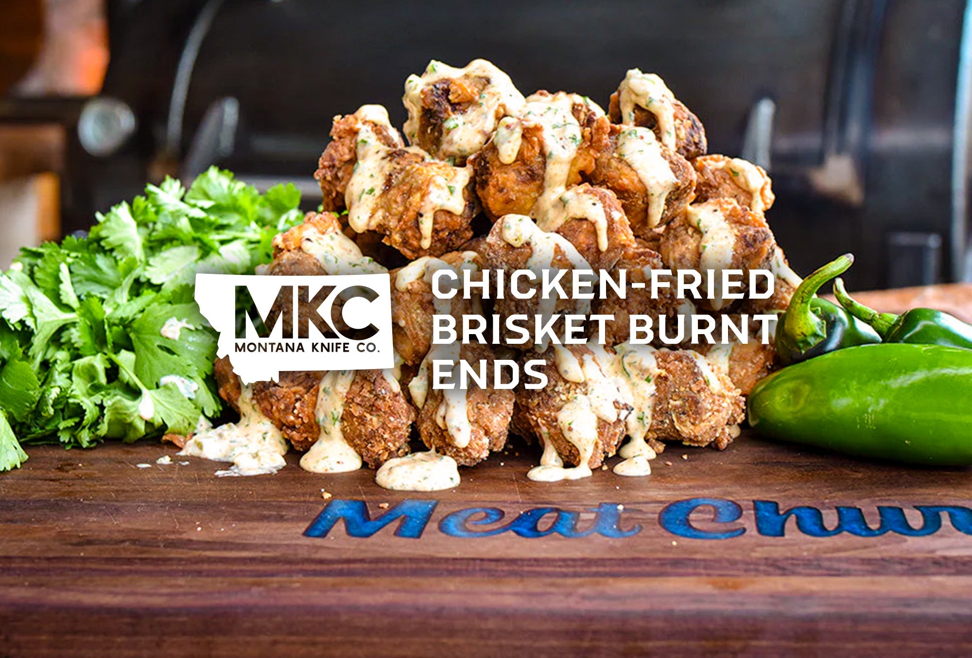 Close-up of chicken‑fried brisket burnt ends drizzled with creamy sauce, with peppers and herbs arranged beside them.