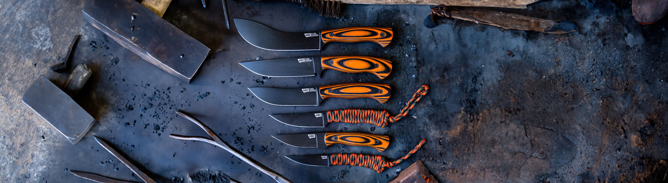 A collection of Montana Knife Company knives with orange and black handles displayed on a rugged surface, showcasing craftsmanship.