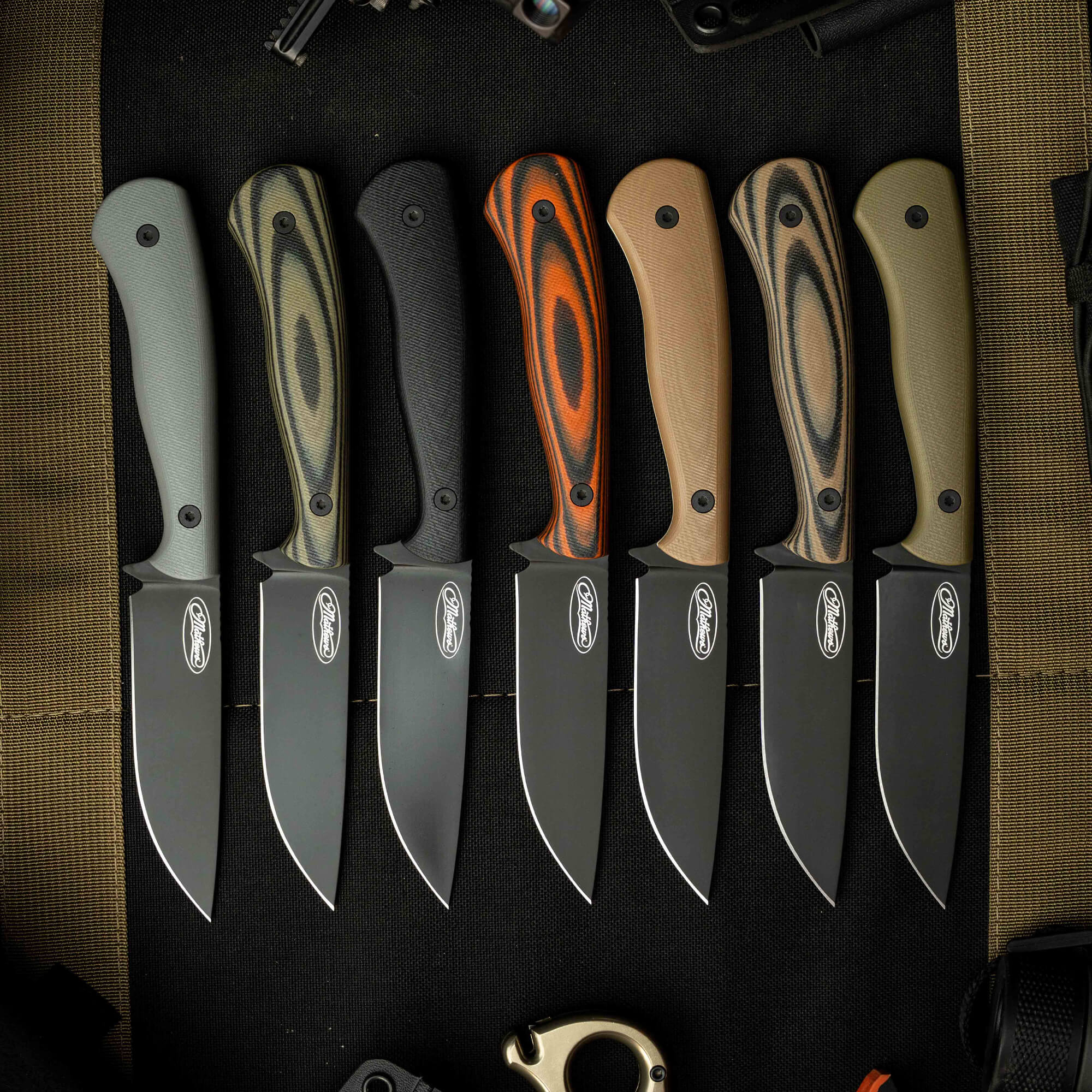 A collection of eight MKC Whitetail knives with various handle colors and textures, showcasing their sleek, durable blades.