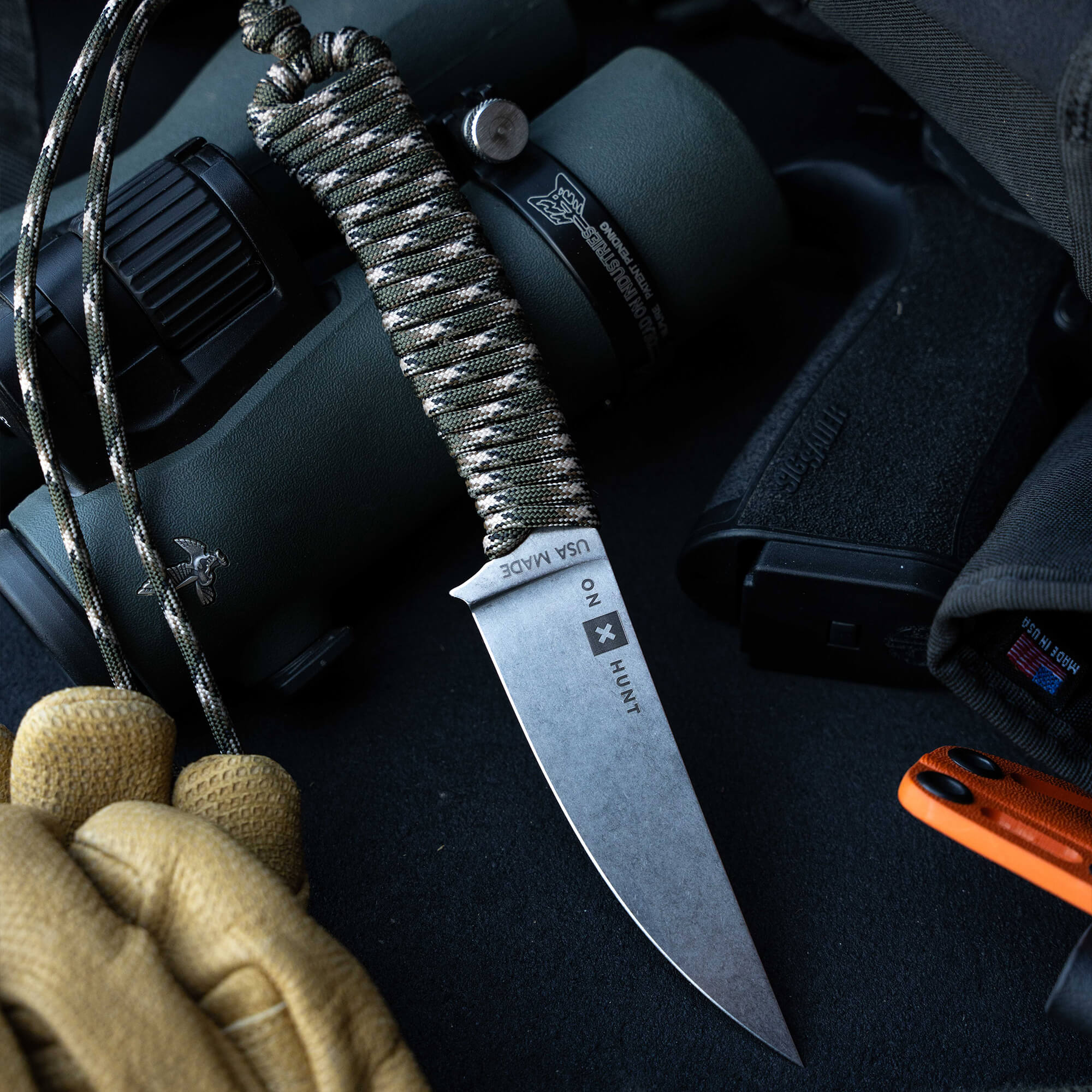 ONX Hunt Magnacut Speedgoat 2.0 knife with paracord handle beside binoculars and gloves, ideal for outdoor enthusiasts.