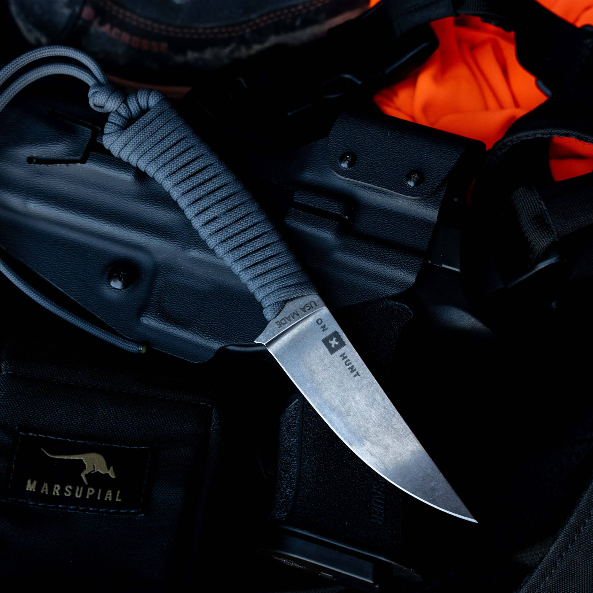 ONX Hunt Magnacut Speedgoat 2.0 knife with a gray paracord handle resting on tactical gear and a black holster.