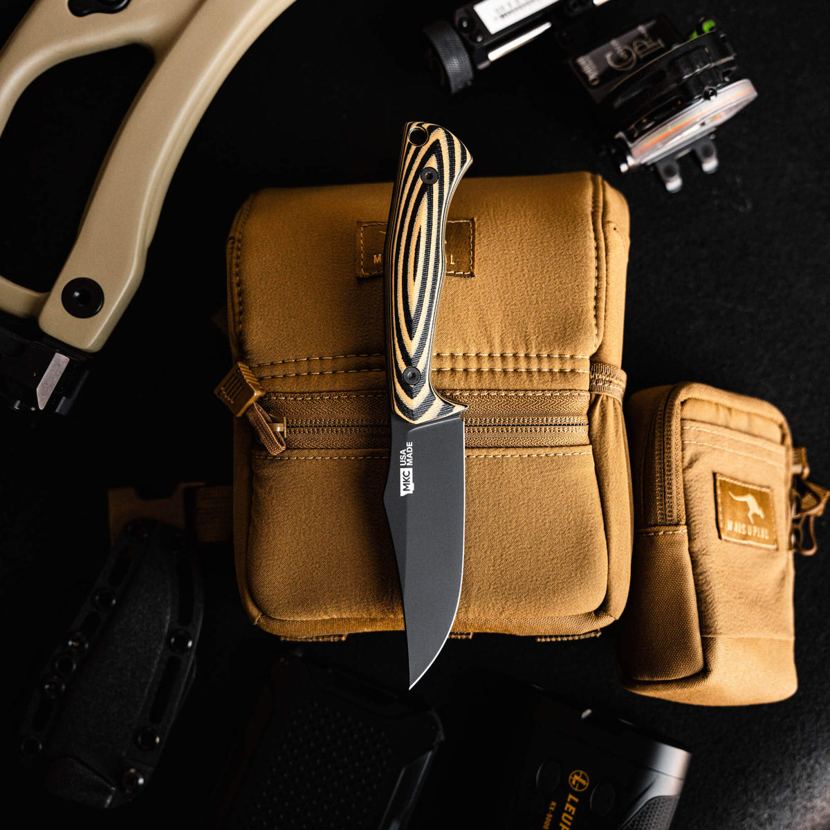 Triumph Pro knife in tan and black with a sleek blade, surrounded by tactical gear and a storage pouch.