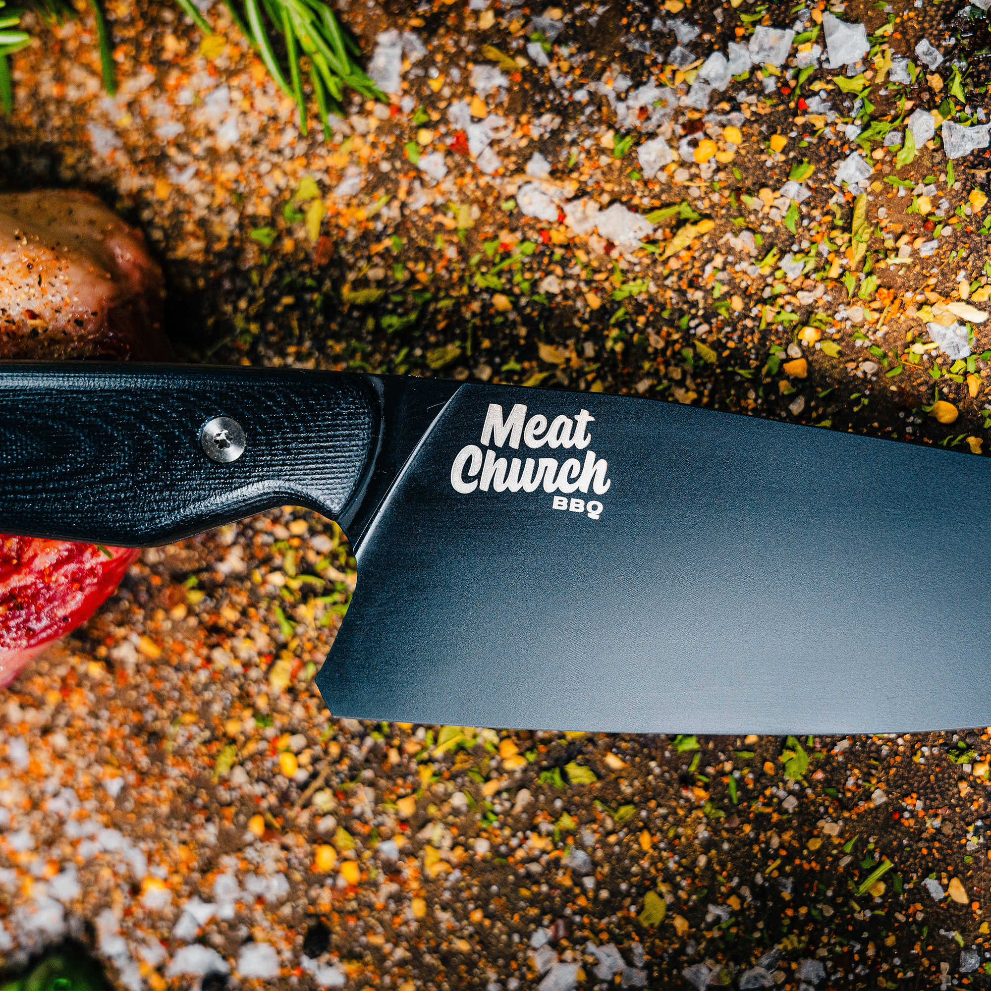 High-quality Meat Church chef knife with a sleek black blade and ergonomic handle, surrounded by spices and fresh ingredients.