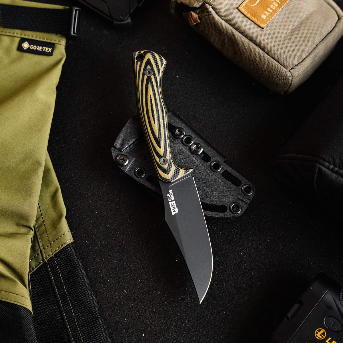 Triumph Pro knife in green and black with a sleek blade, resting on a tactical background of gear and accessories.