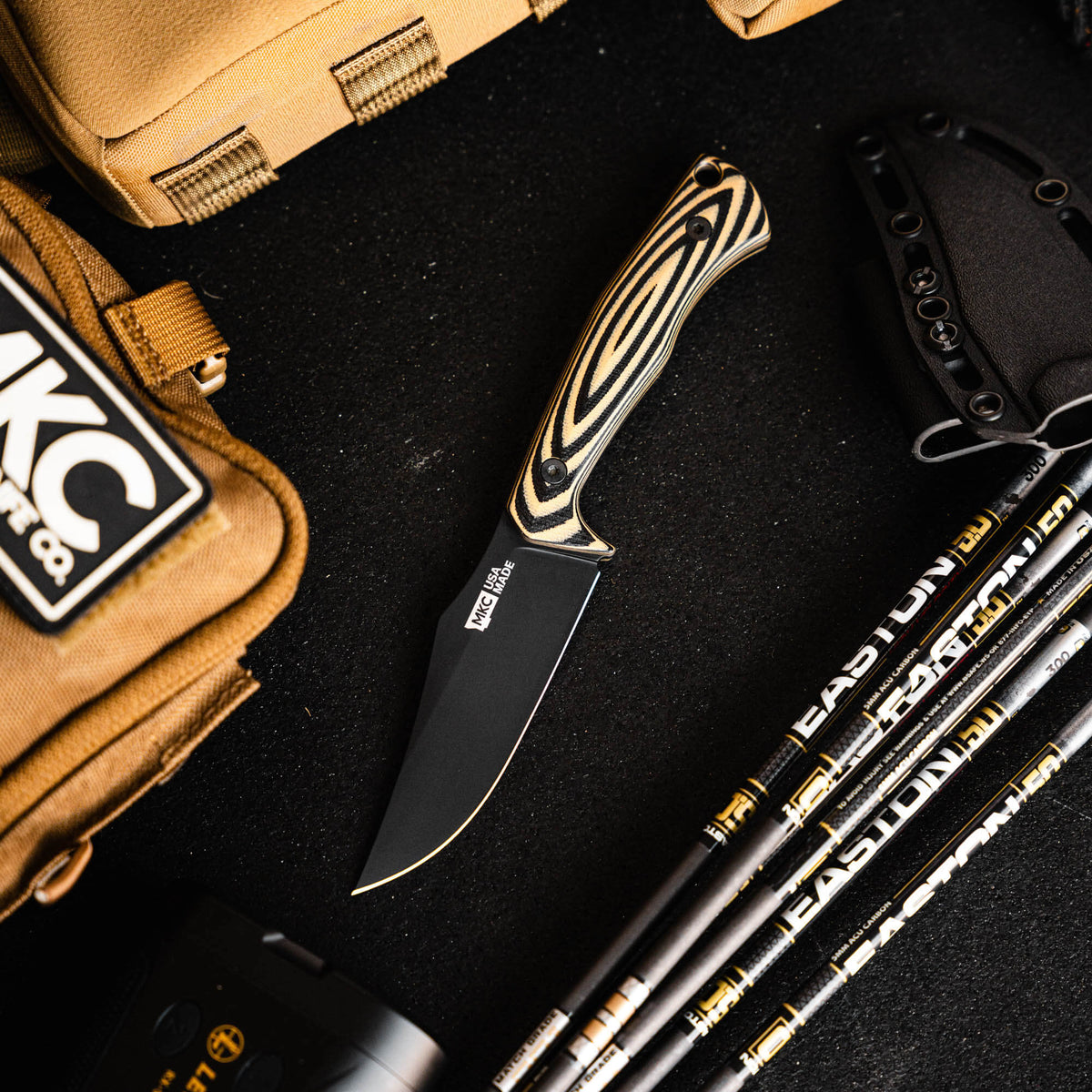 Montana Knife Company's Triumph Pro knife in tan and black, featuring a sleek blade and ergonomic handle, surrounded by gear.