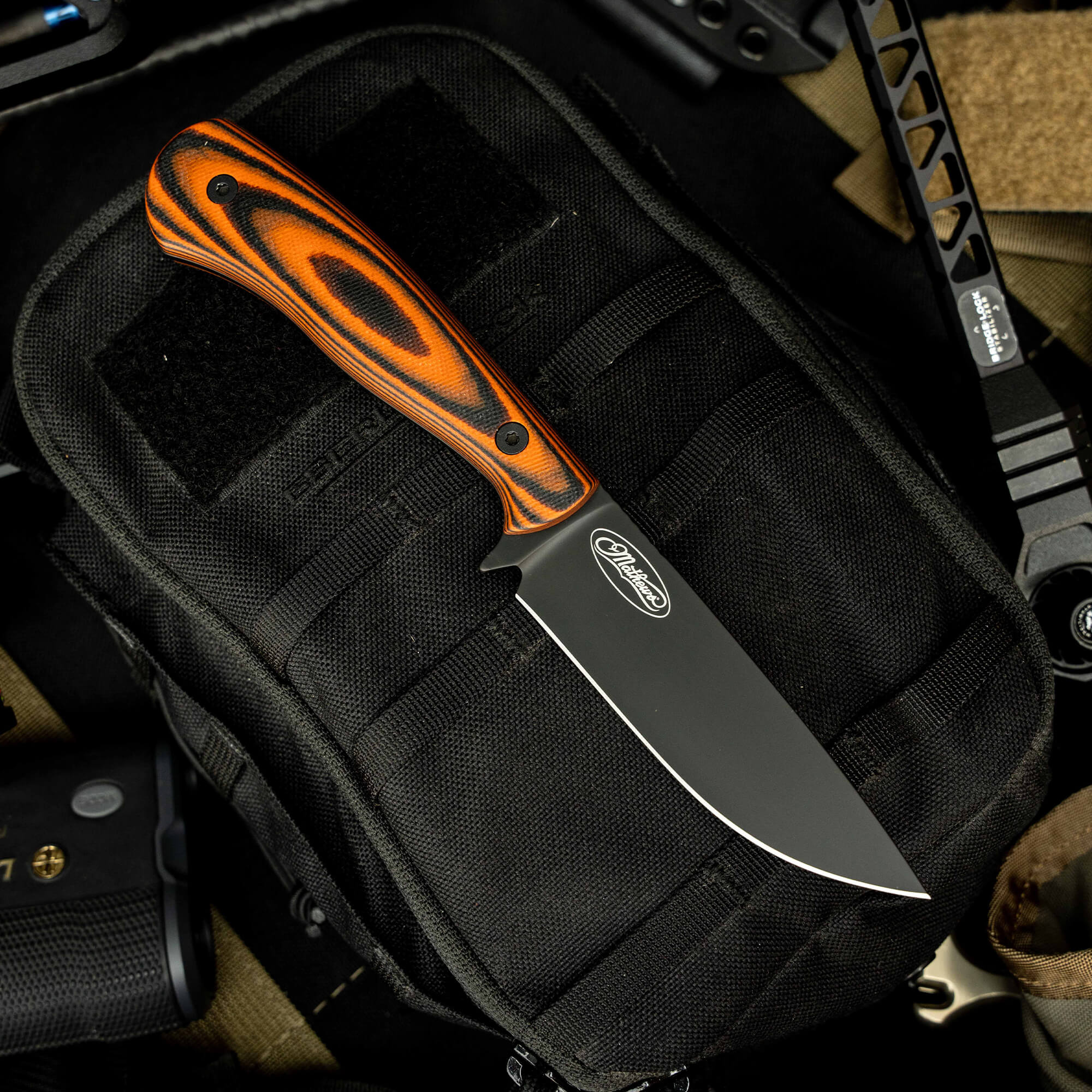 Mathews Archery MKC Whitetail knife with a black blade and orange patterned handle on a tactical pouch.