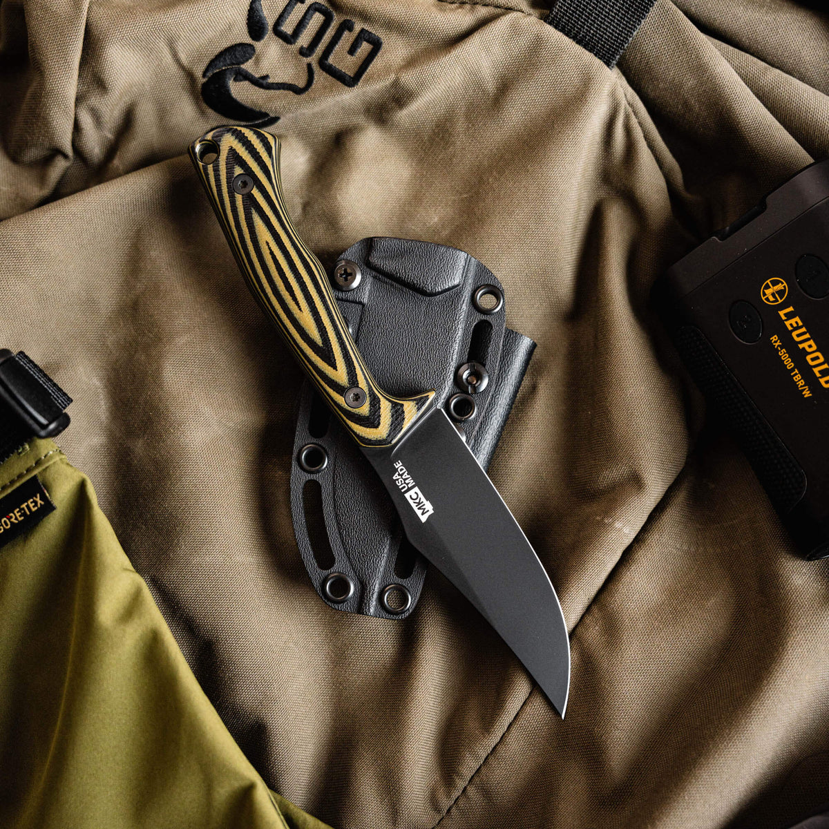 Triumph Pro knife in green and black with a textured handle, displayed in a sheath on a fabric background.