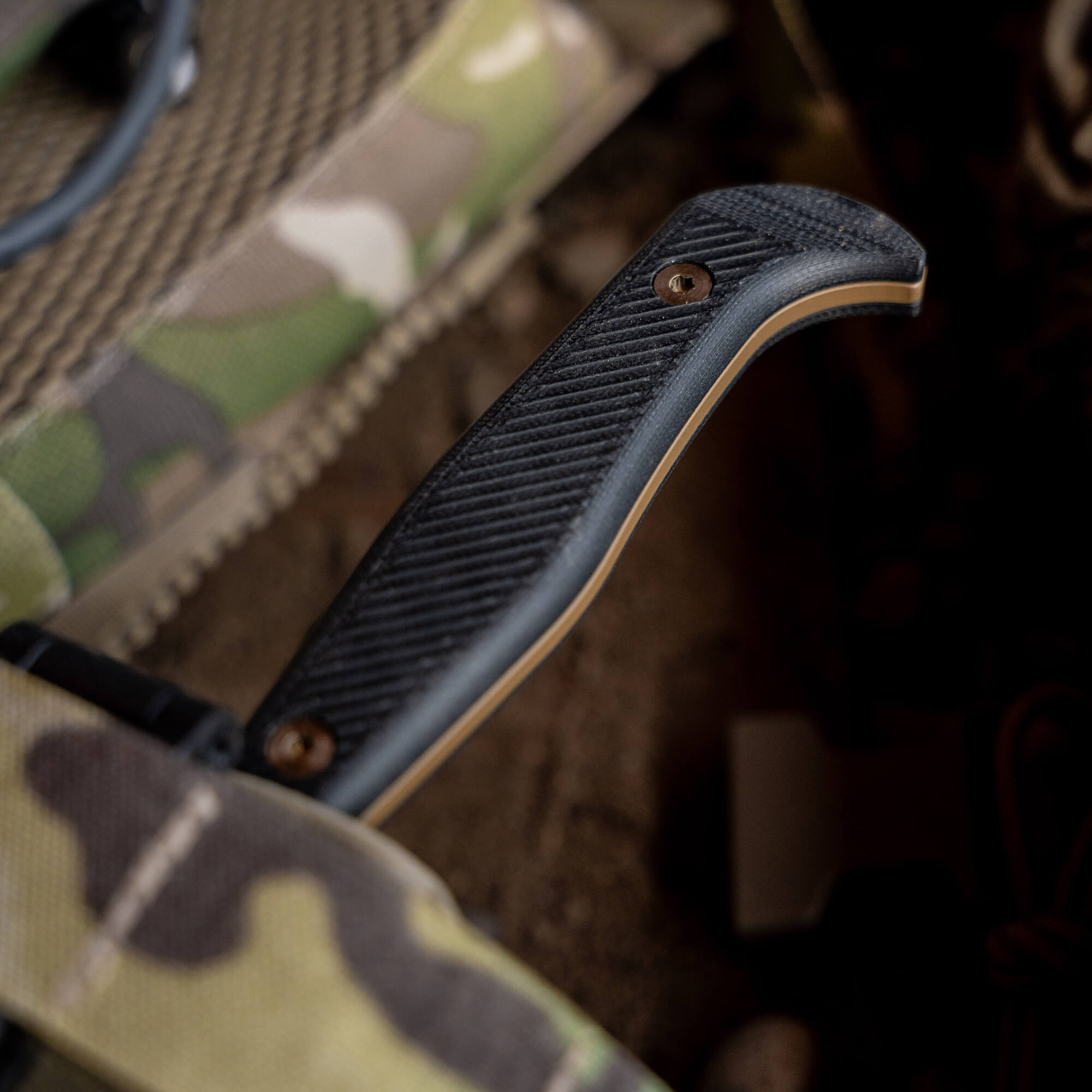 Close-up of a Battle Goat knife with a textured coyote black handle resting on a camouflage background, showcasing outdoor utility design elements.
