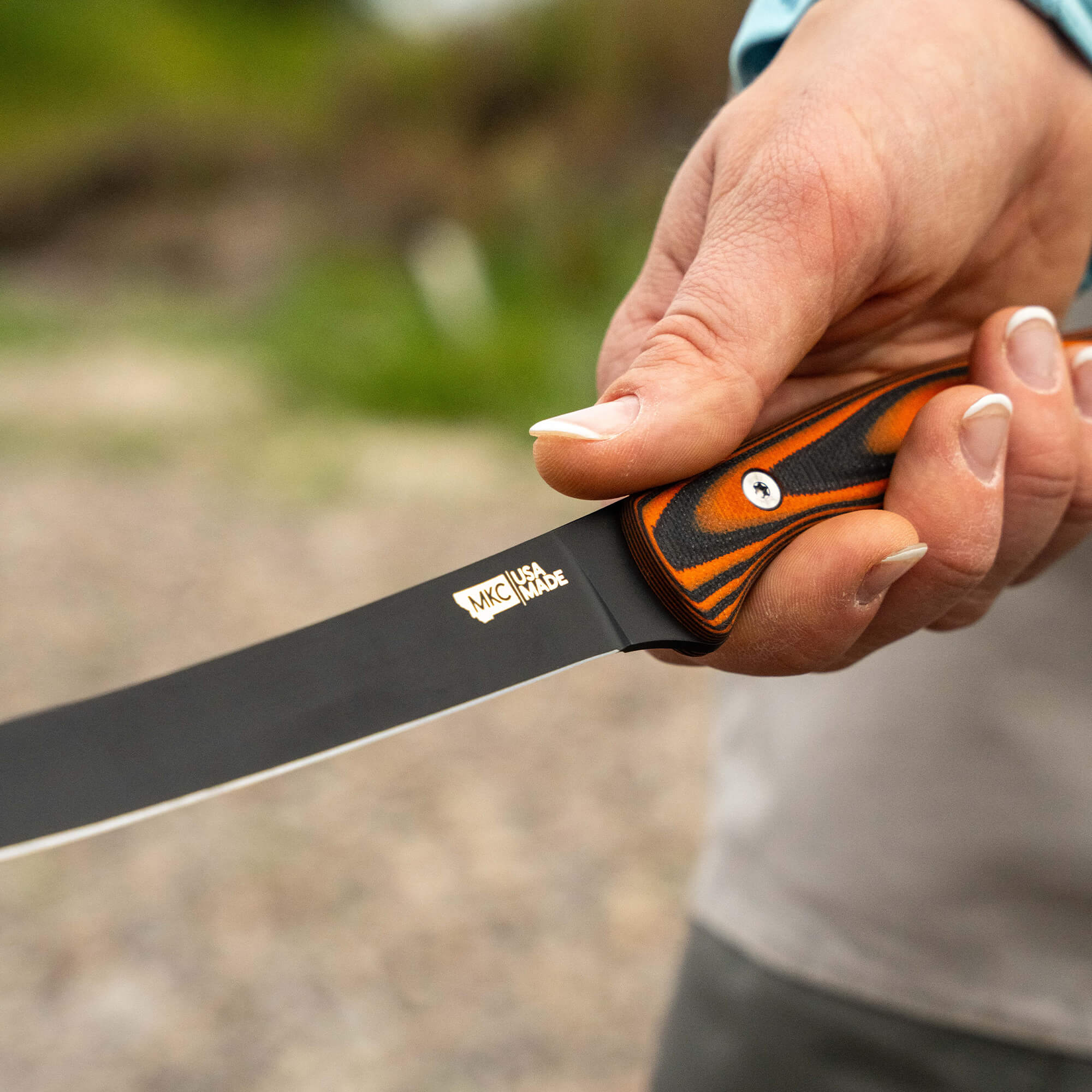 Hand holding the HUK Flathead Fillet knife with a sleek black blade and an orange and black handle, ideal for fishing.