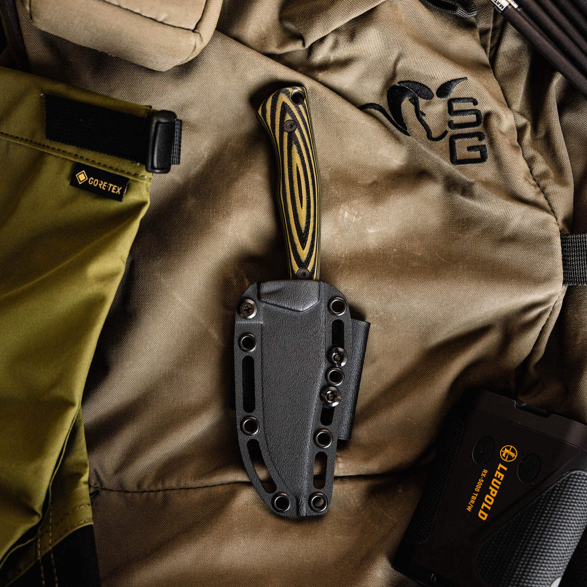 Triumph Pro knife in green and black with a textured handle, resting in a tactical gear setting.