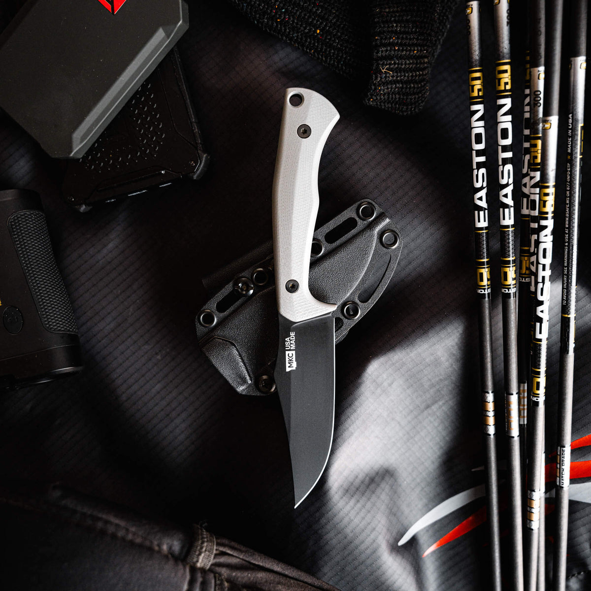 Grey Triumph Pro knife with a fixed blade and ergonomic handle, displayed on a textured black background with gear.