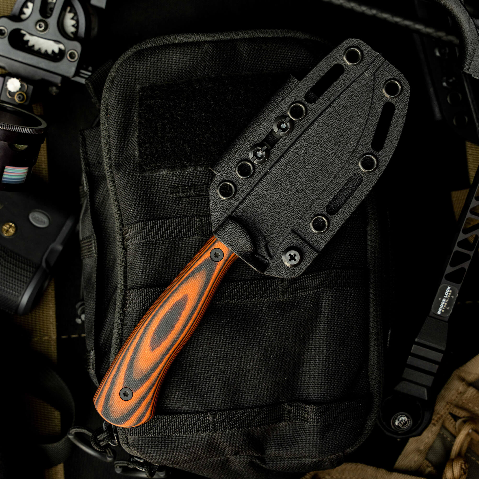 Mathews Archery MKC Whitetail knife with a black sheath and orange handle, resting on tactical gear.