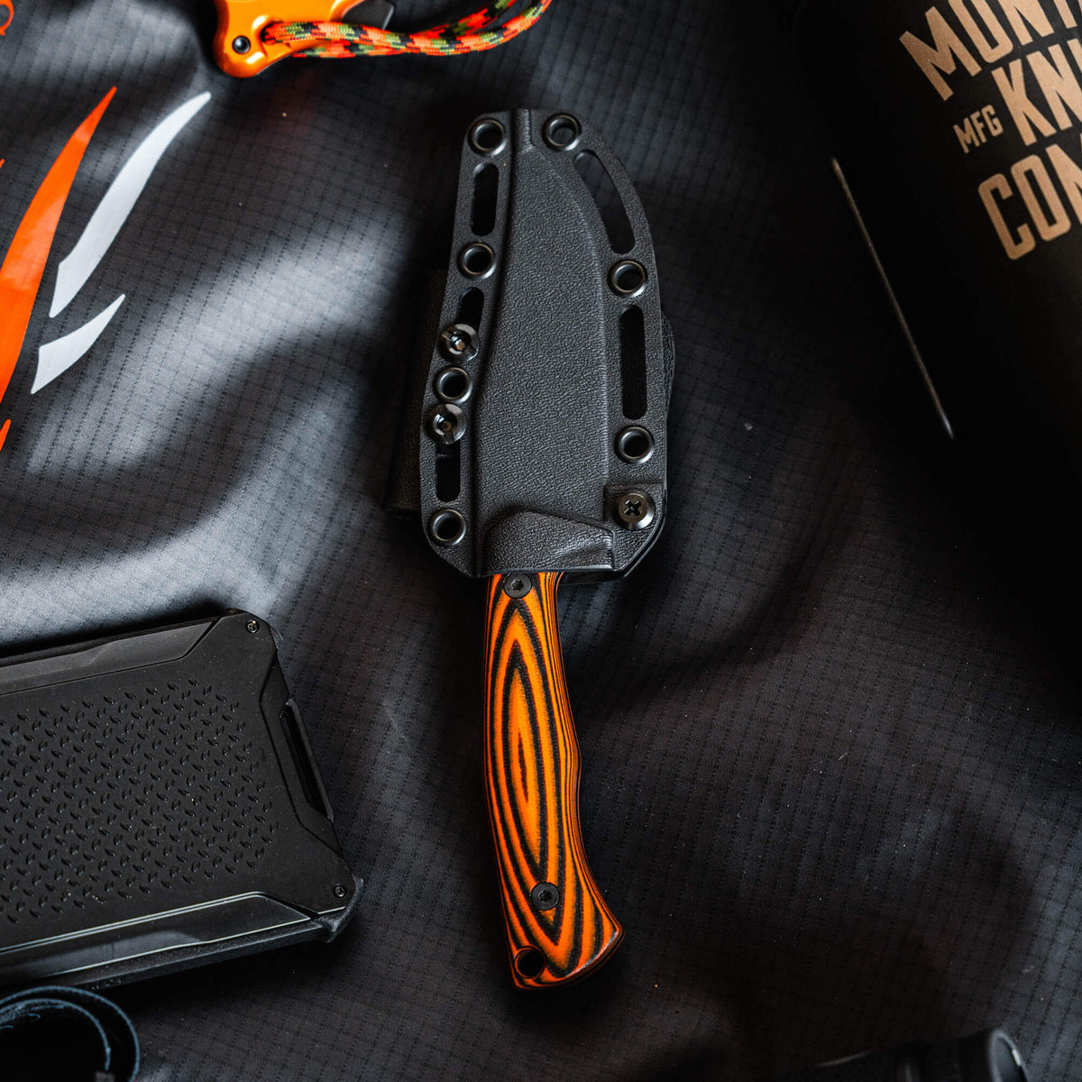 Triumph Pro knife with an orange and black handle, featuring a durable sheath, ideal for outdoor and tactical use.