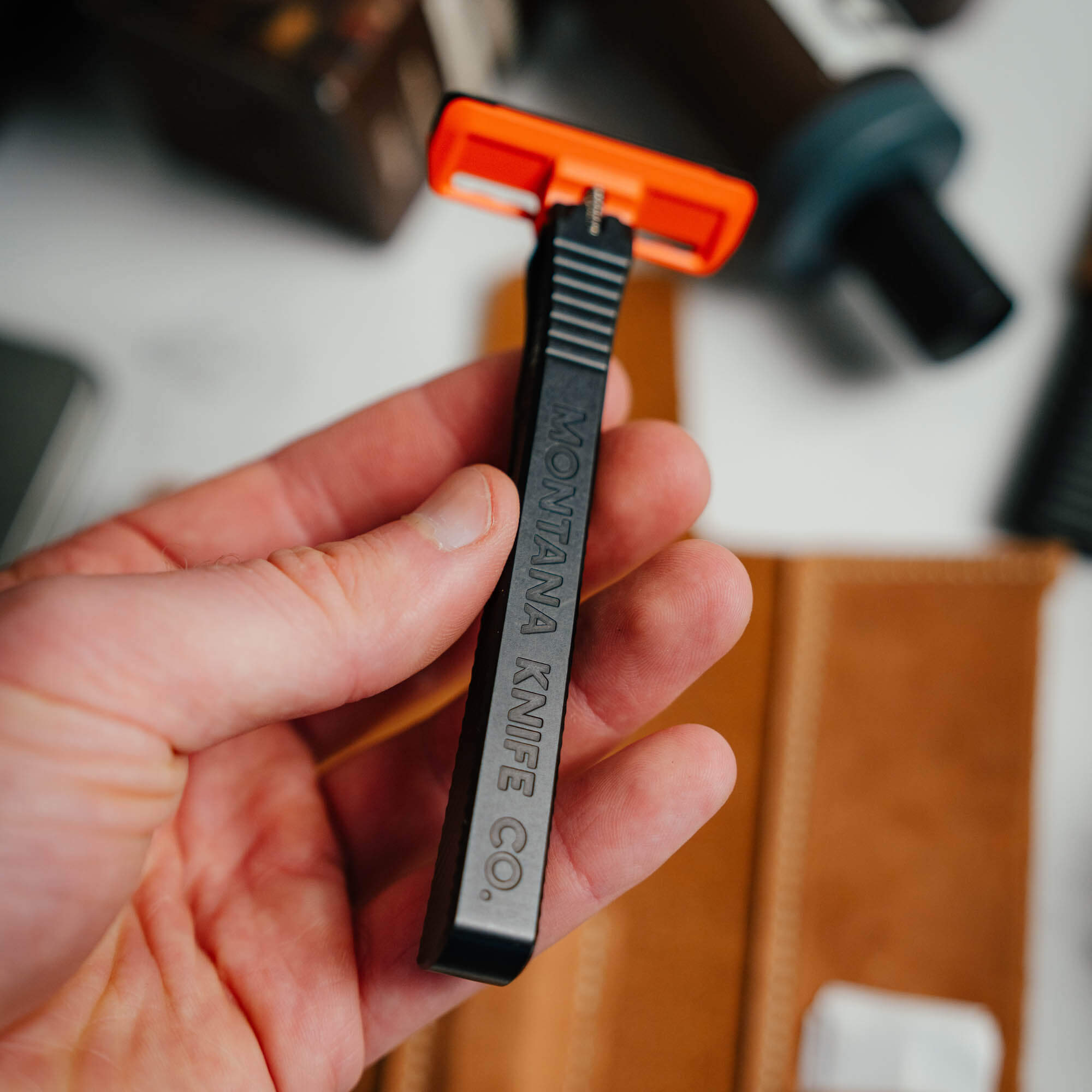 EDC Razor 2.0 by Montana Knife Company, featuring a sleek black handle and bright orange safety guard, held in hand.
