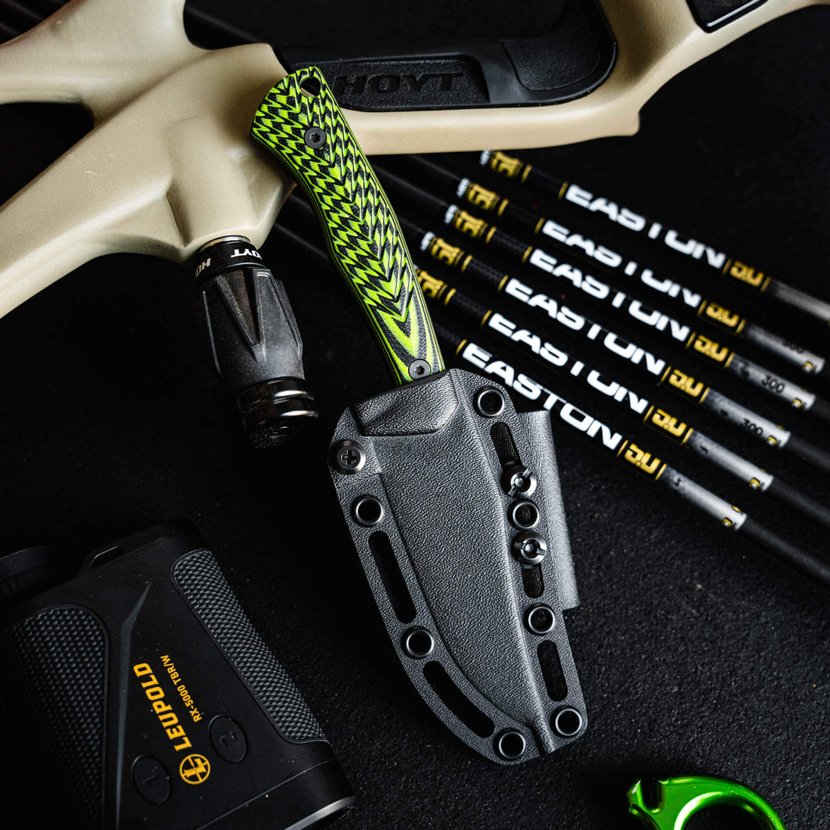 Triumph Pro knife with neon green and black handle, displayed with archery equipment and accessories.