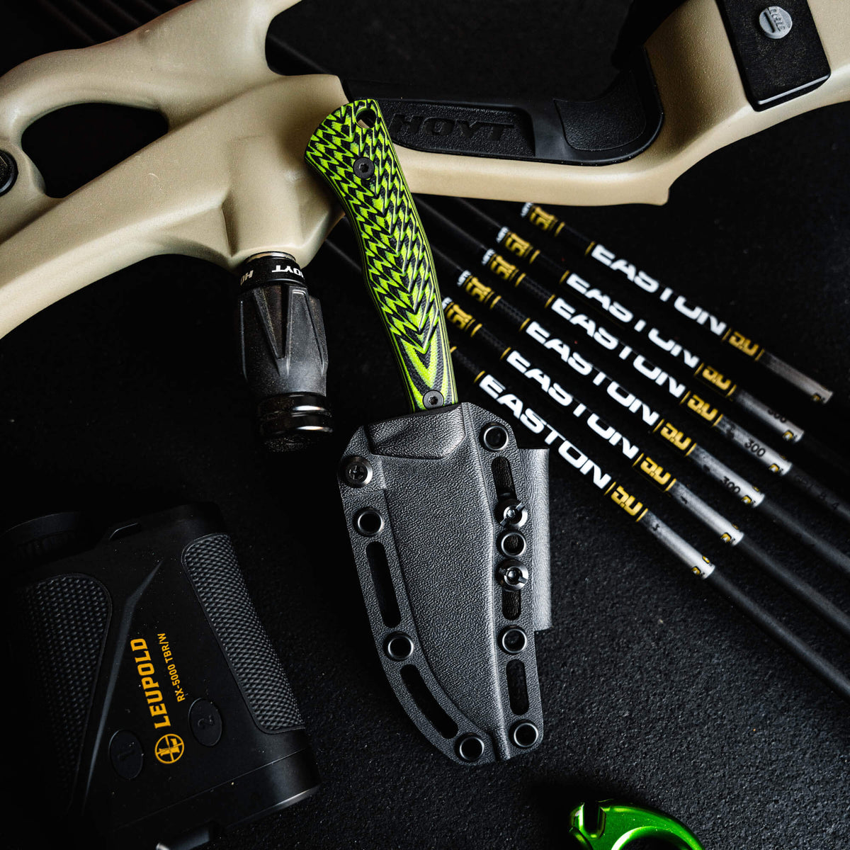 Triumph Pro knife in neon green and black with a sheath, surrounded by archery equipment and a rangefinder.