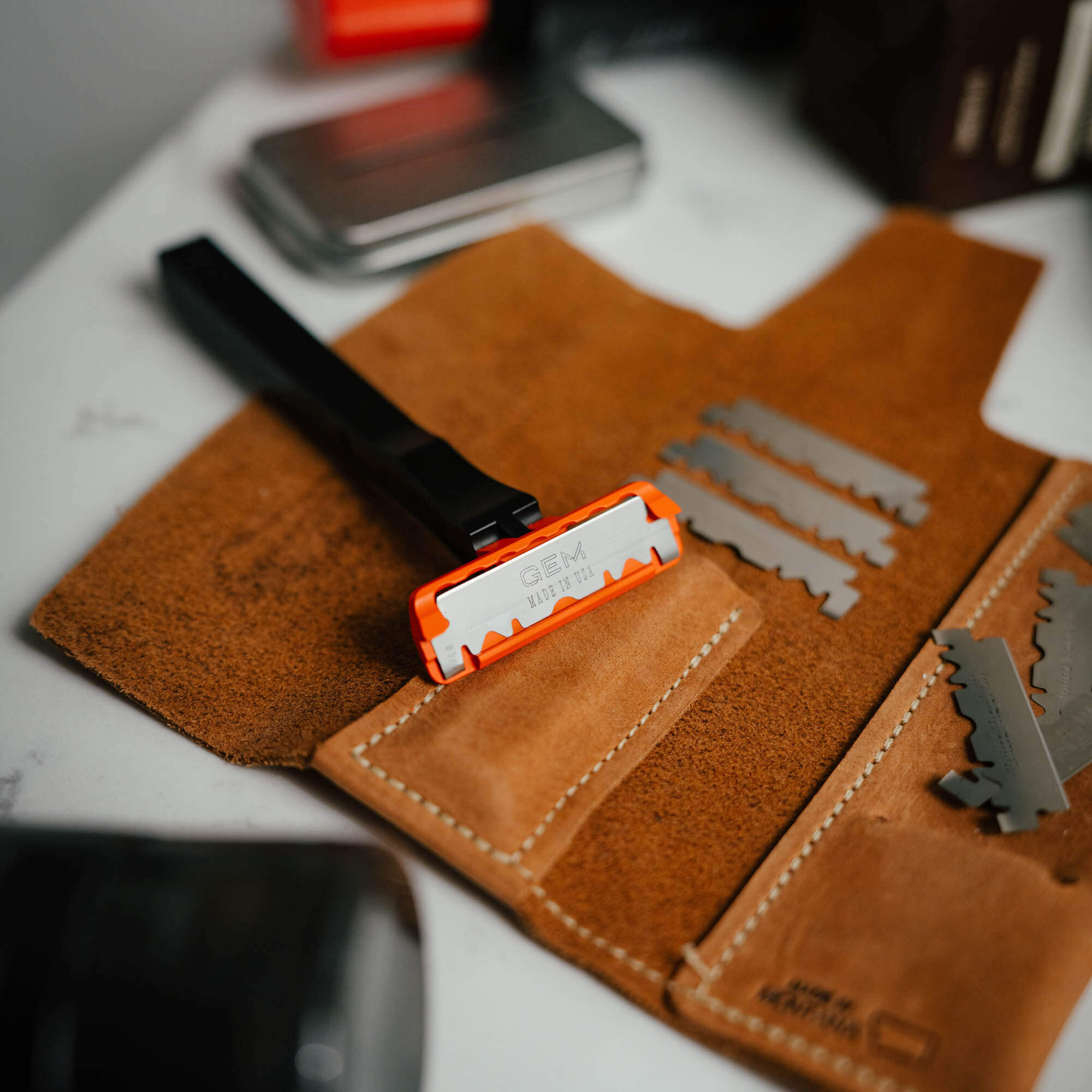 EDC Razor 2.0 with orange blade holder on a leather pouch, showcasing replacement blades for versatile cutting tasks.
