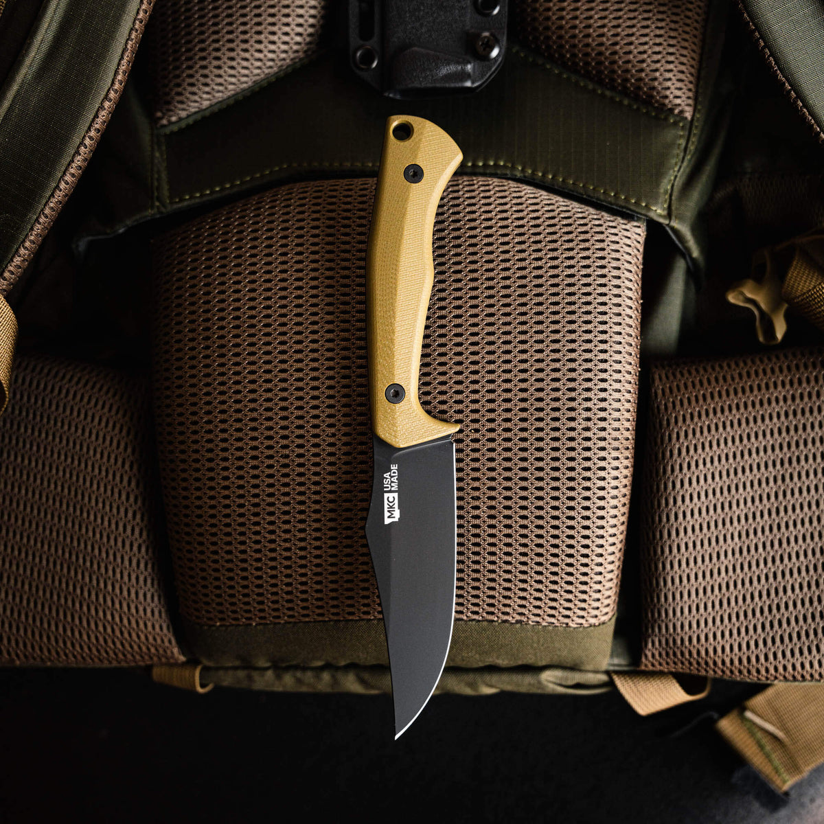 Olive green Triumph Pro knife with a textured handle, resting on a tactical backpack's padded surface.