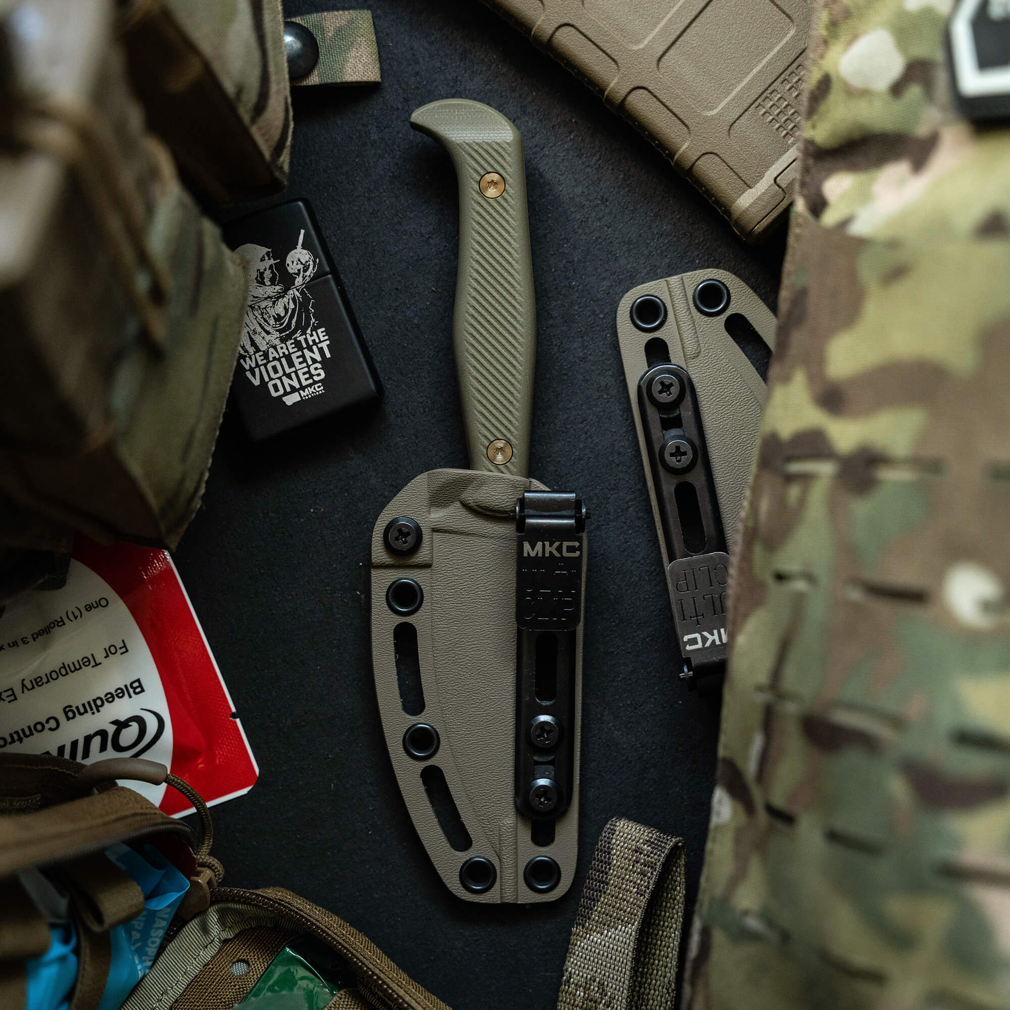 Alt text: "Close-up view of a tactical fixed-blade knife, the BATTLE GOAT - COY/OD, with a coyote tan handle and matching sheath amidst other military gear, including a GPS device, tactical patches, and