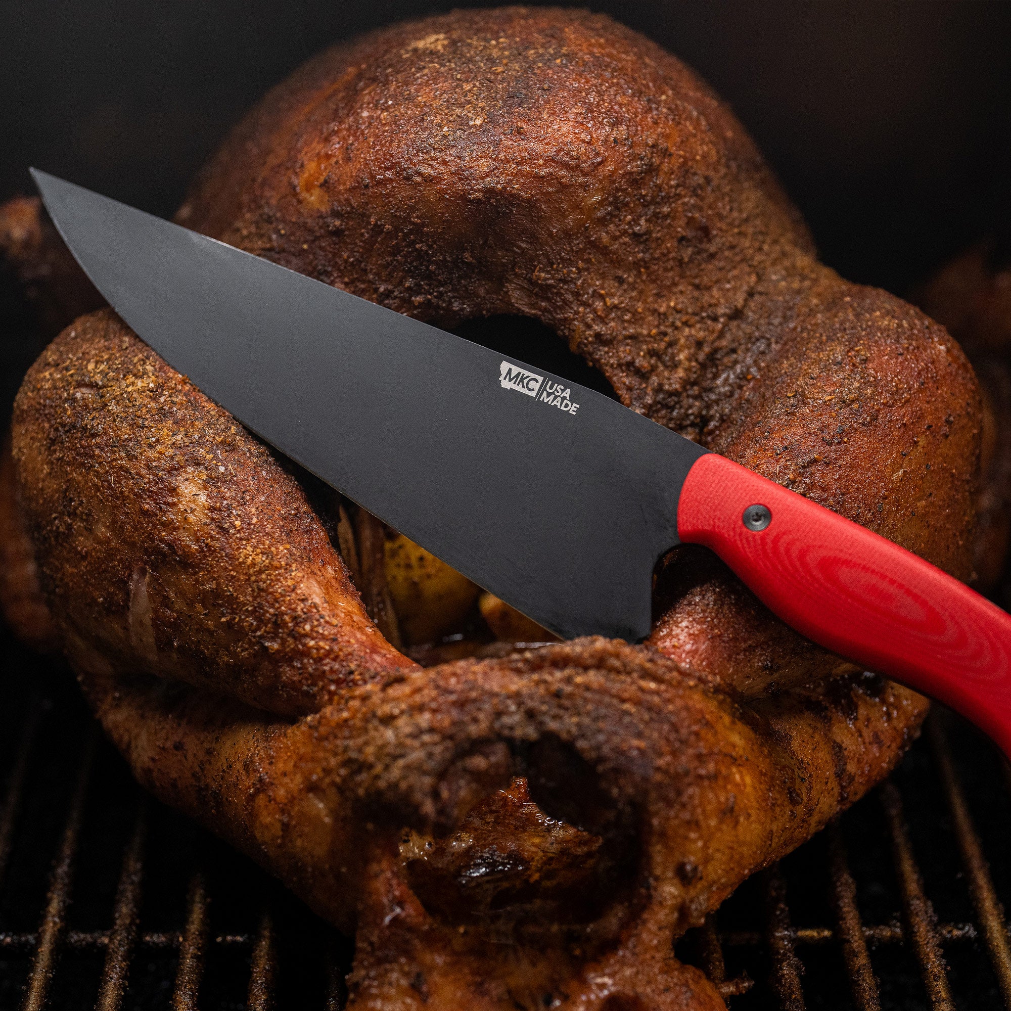 Red-handled Bighorn Chef knife cutting into a well-seasoned roasted chicken on a grill.