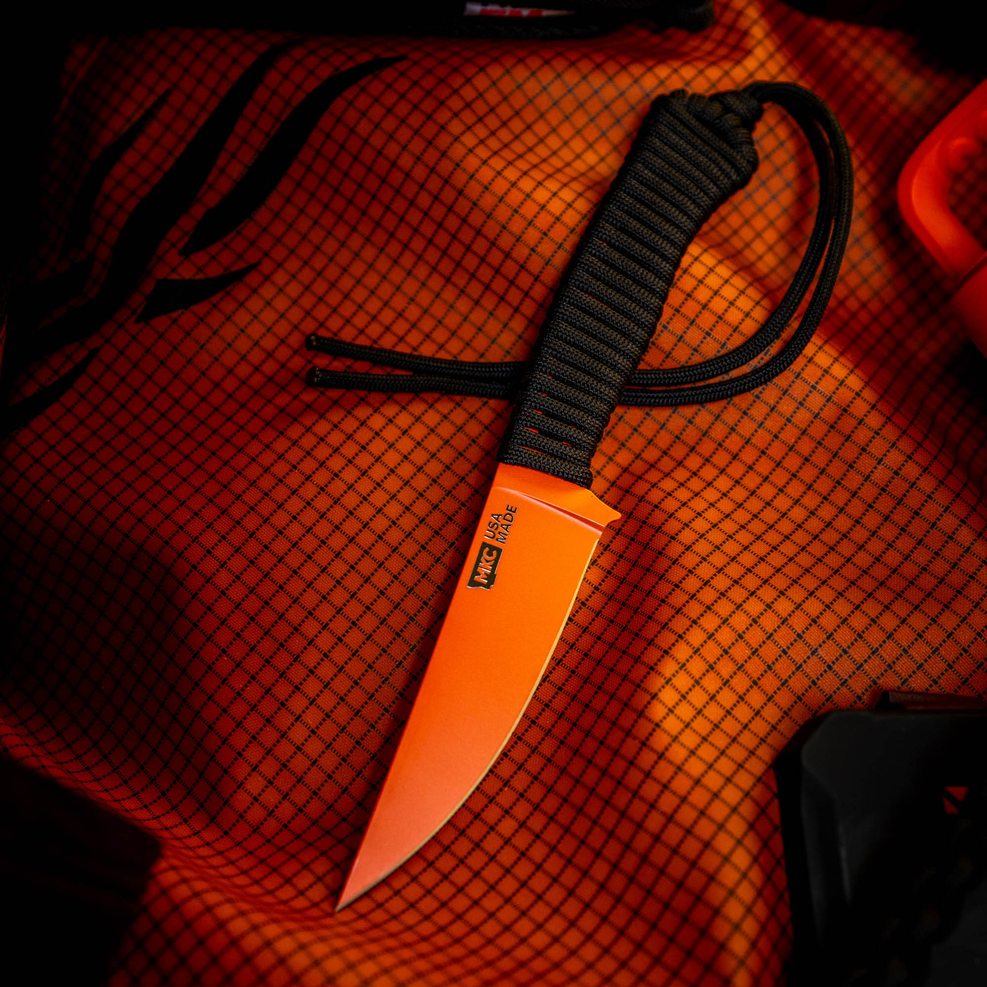 SPEEDGOAT 2.0 knife with blaze orange Cerakote finish on a textured orange background, featuring a paracord handle.