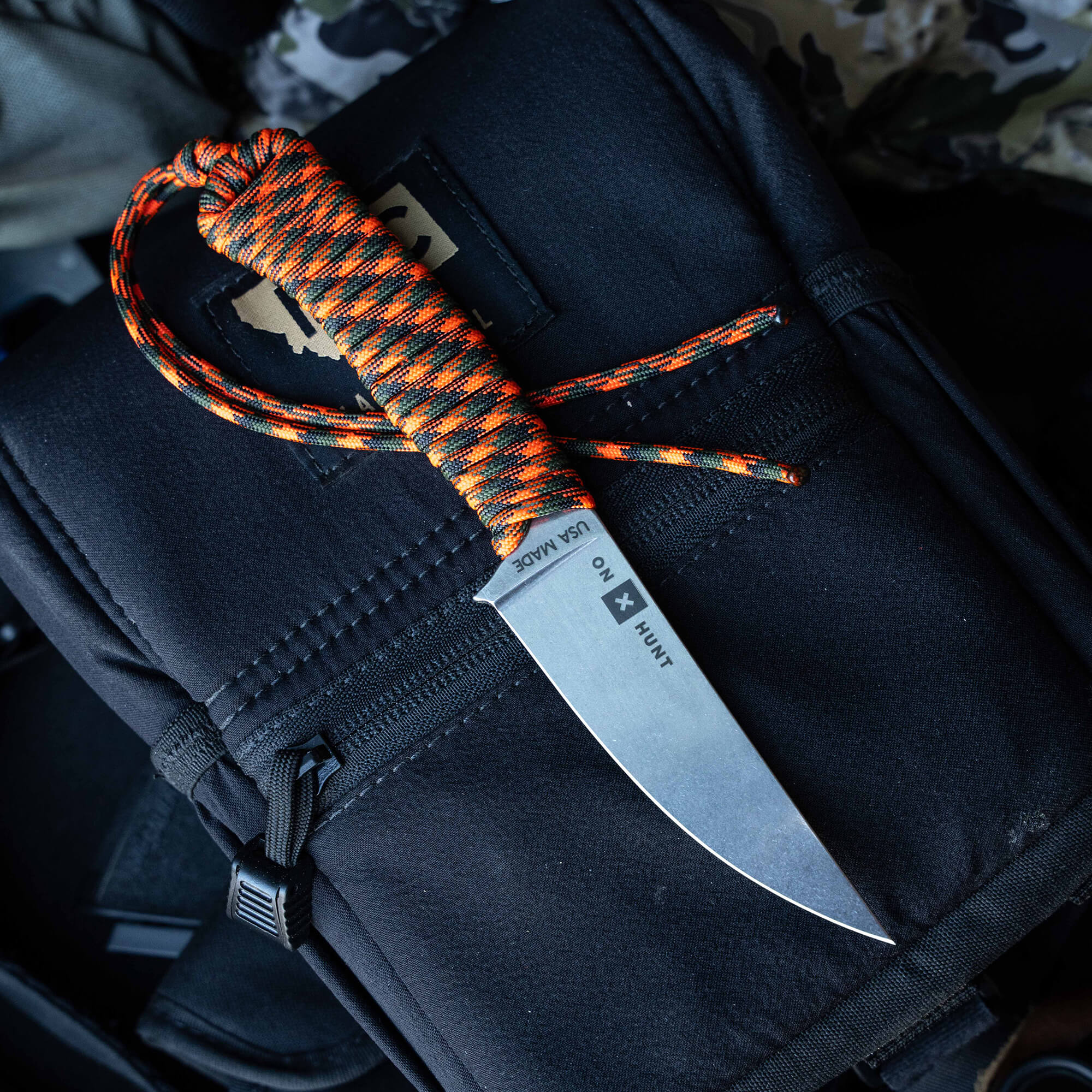 ONX Hunt Magnacut Speedgoat 2.0 knife with orange and black paracord handle on a tactical bag background.