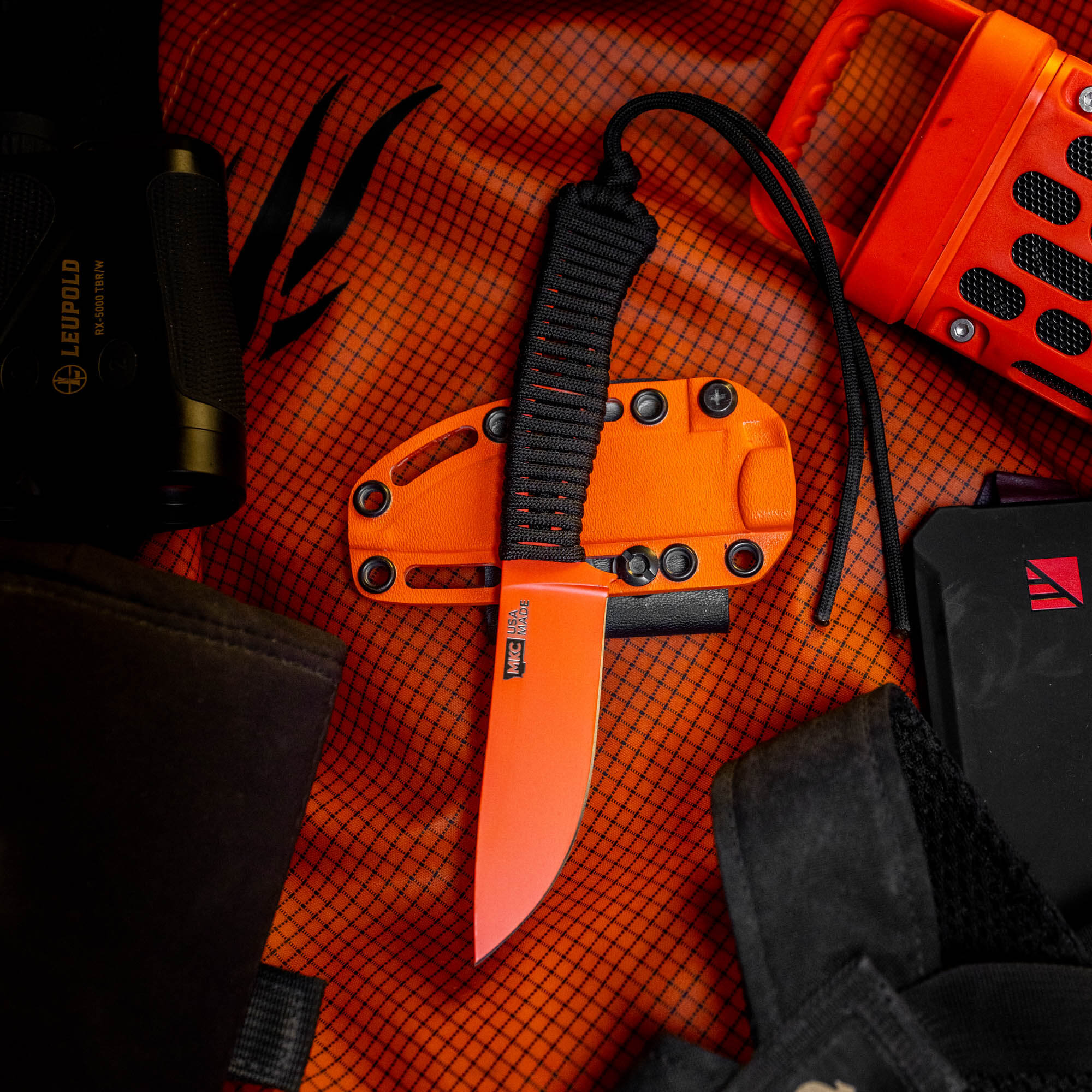 Blaze orange Cerakote STONED GOAT 2.0 knife on a textured background with tactical gear, showcasing its rugged design.