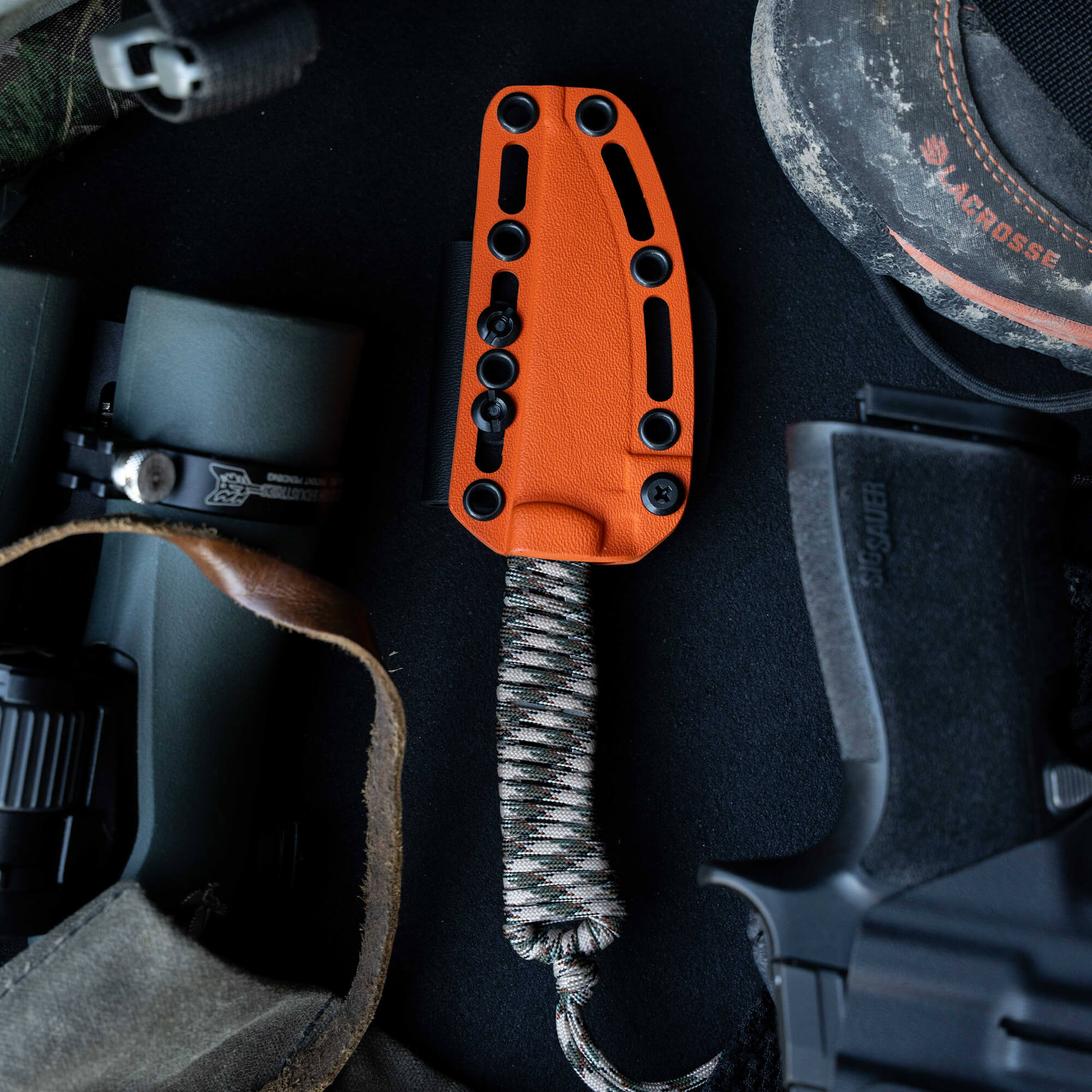 ONX Hunt Magnacut Speedgoat 2.0 knife with orange handle and paracord, surrounded by outdoor gear and tools.