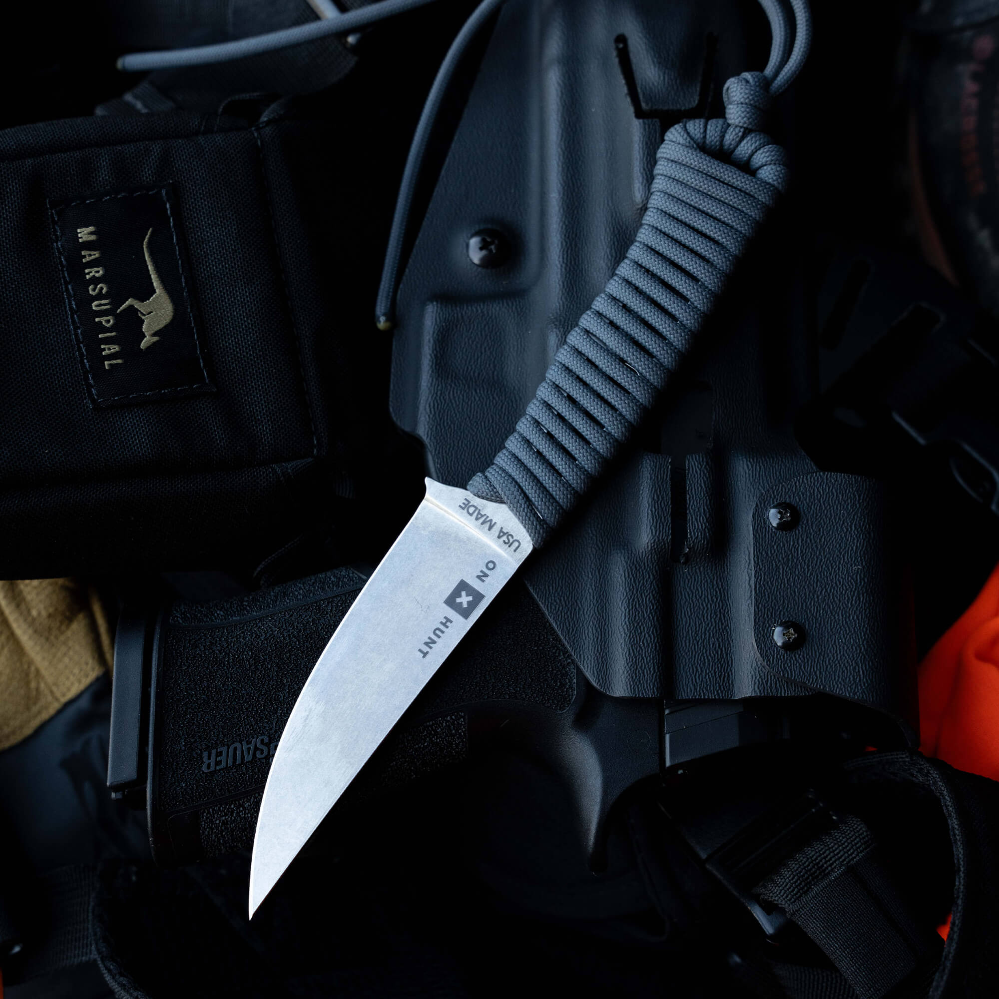ONX Hunt Magnacut Speedgoat 2.0 knife with gray paracord handle, resting on tactical gear and a black holster.