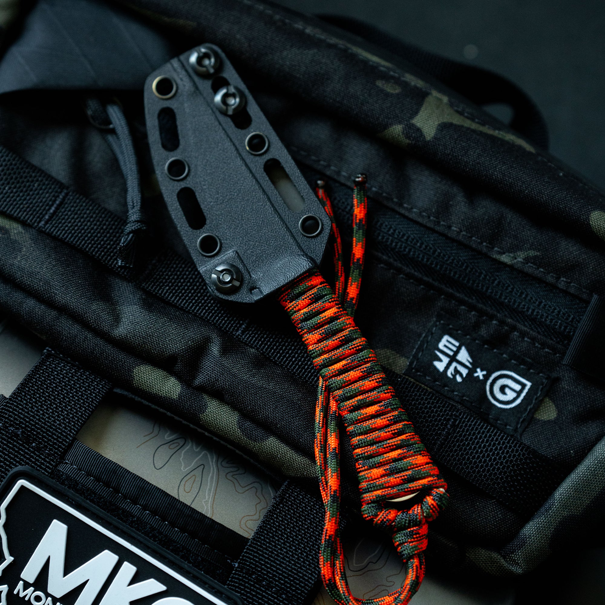 ONX Hunt Mini-Speedgoat 2.0 knife with black blade and paracord handle, resting on a camo-patterned bag.