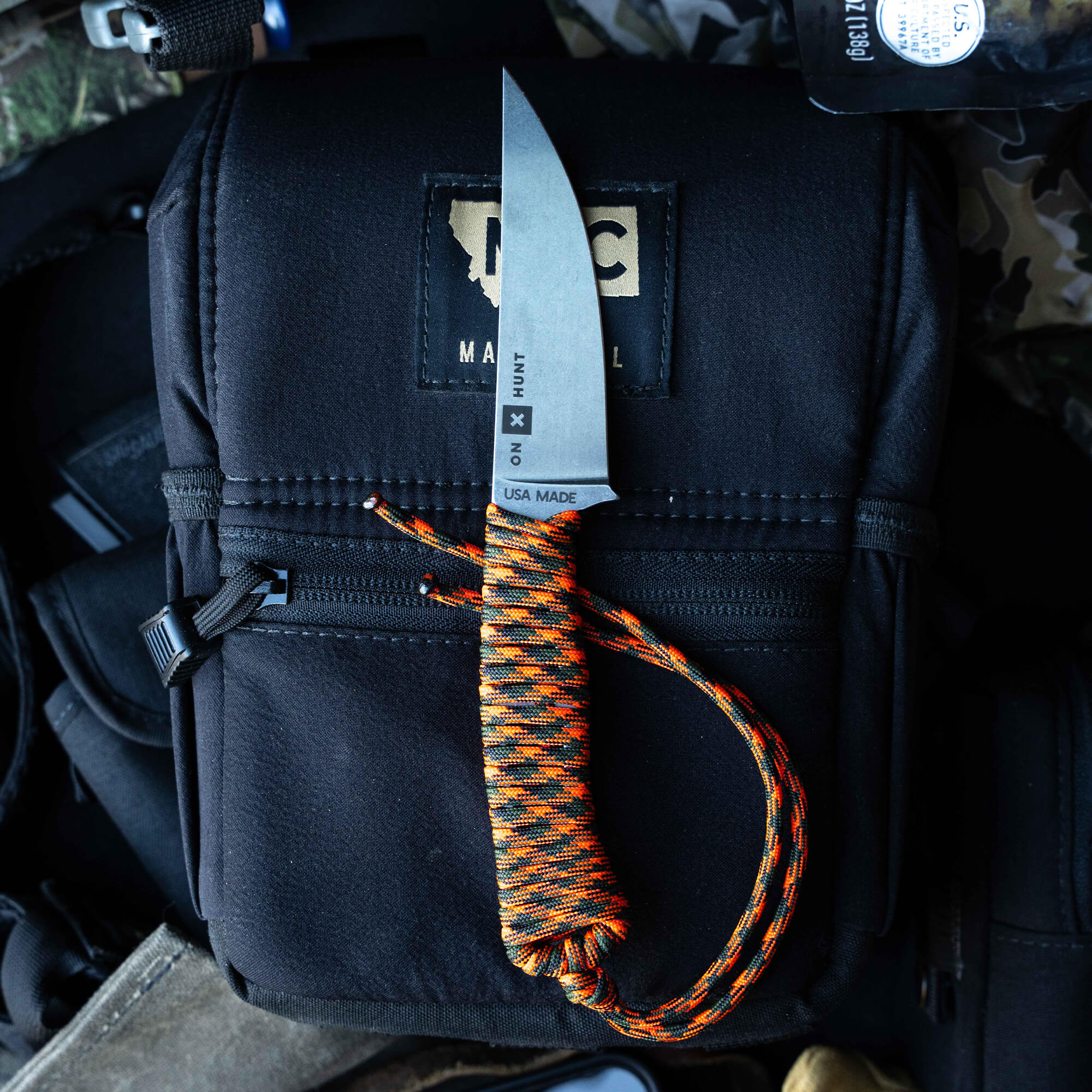 ONX Hunt Magnacut Speedgoat 2.0 knife with a sleek blade and orange-black paracord handle on a tactical bag.
