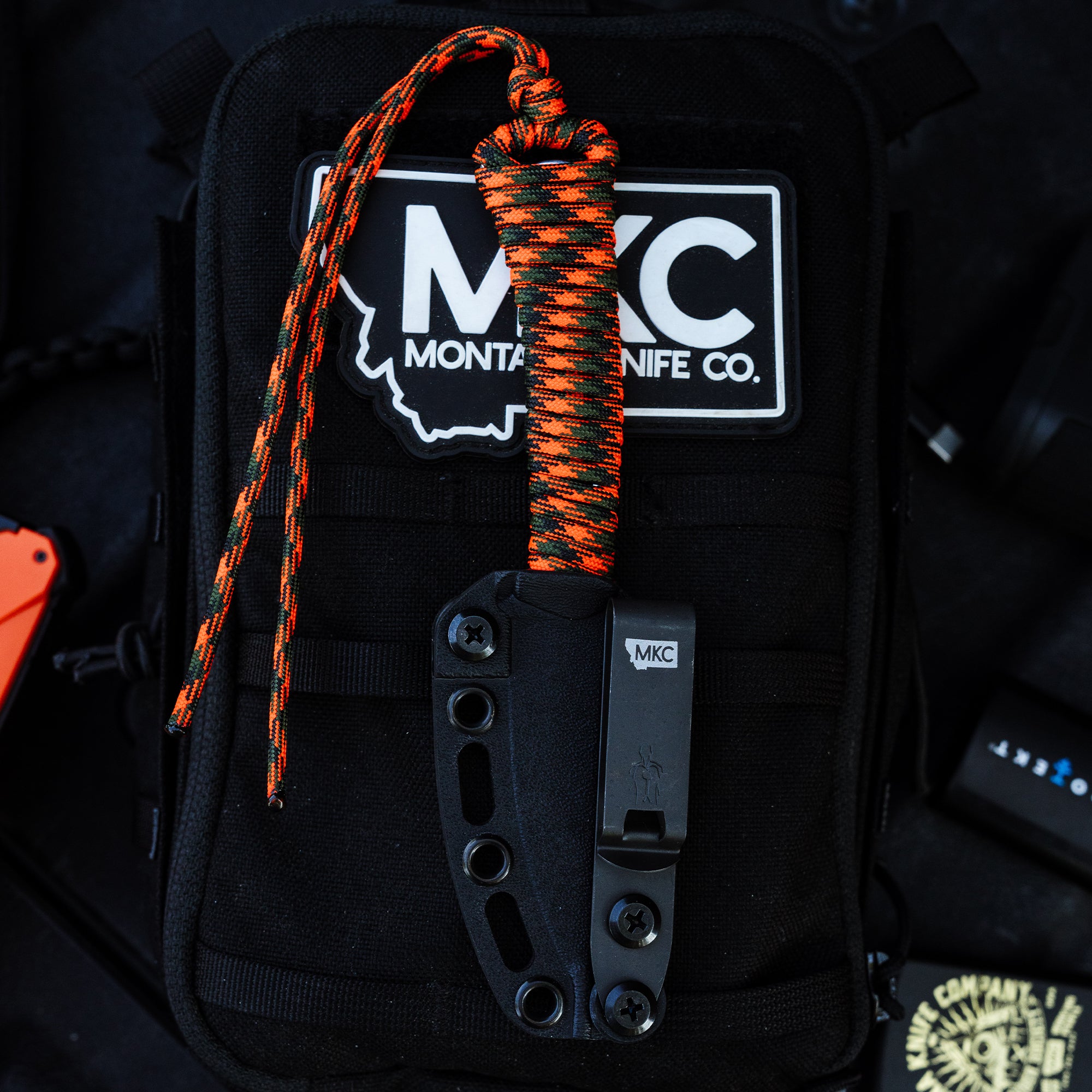 ONX Hunt Mini-Speedgoat 2.0 knife with black and orange paracord on a black tactical bag featuring Montana Knife Company logo.