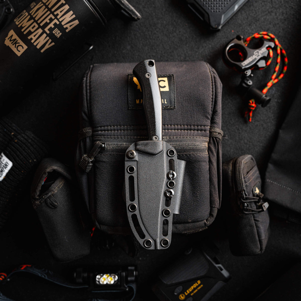 Triumph Pro Black knife displayed on a tactical bag with various outdoor gear, showcasing its durable design and functionality.