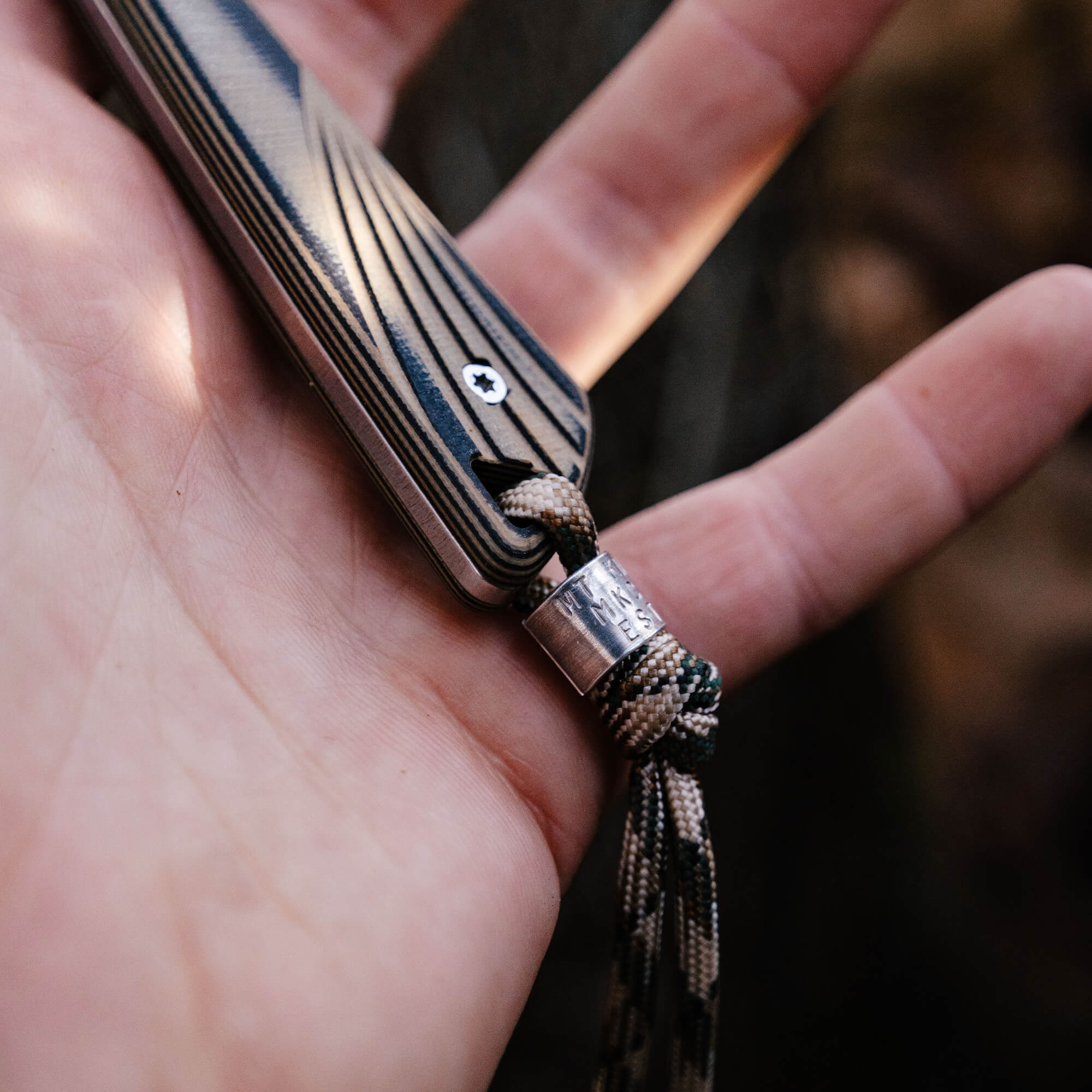 Close-up of the CHÊNE Freezout knife, showcasing its textured handle and lanyard in a hand, highlighting craftsmanship.