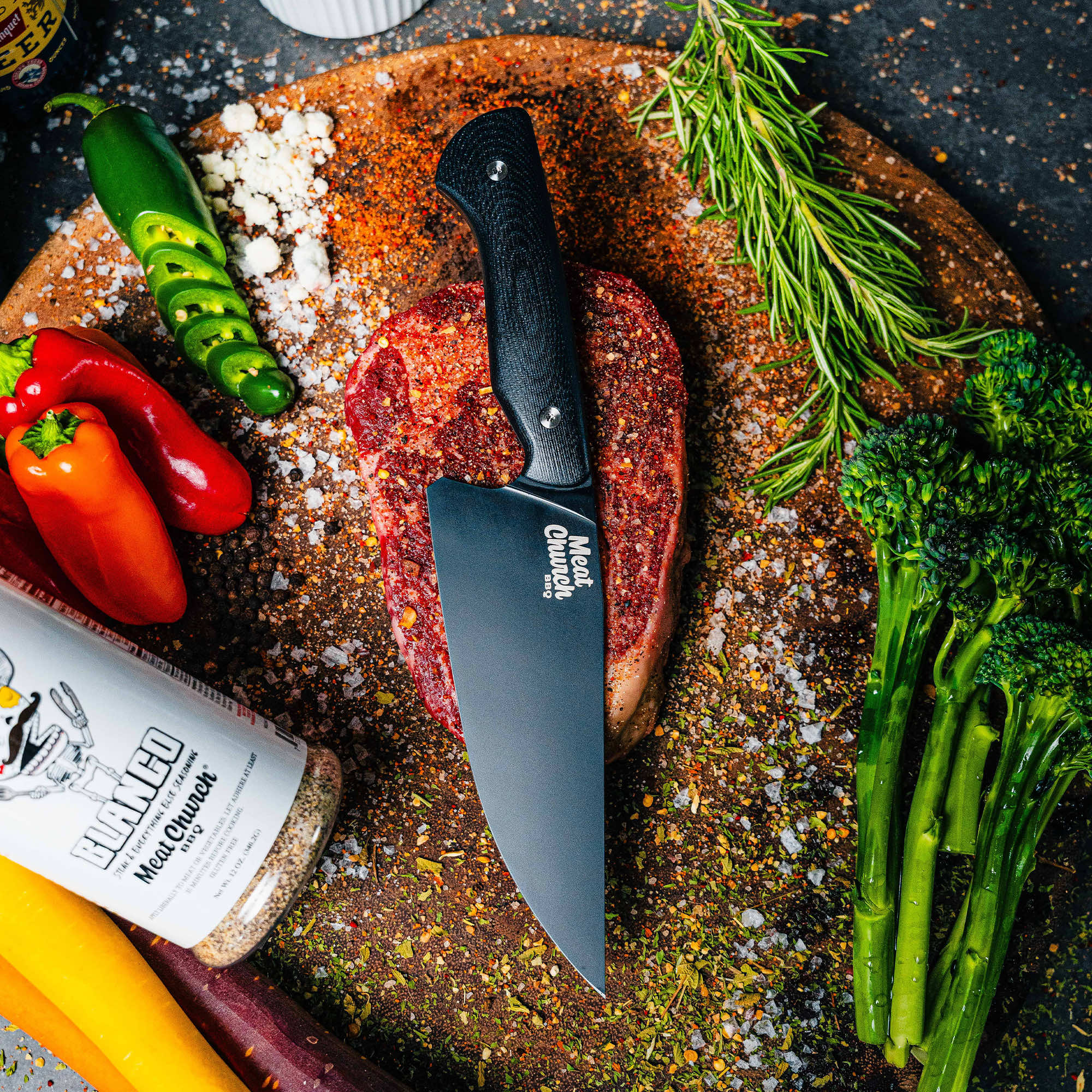Meat Church Chef Knife on a wooden cutting board with fresh vegetables, herbs, and a seasoned steak, showcasing its sharp design.
