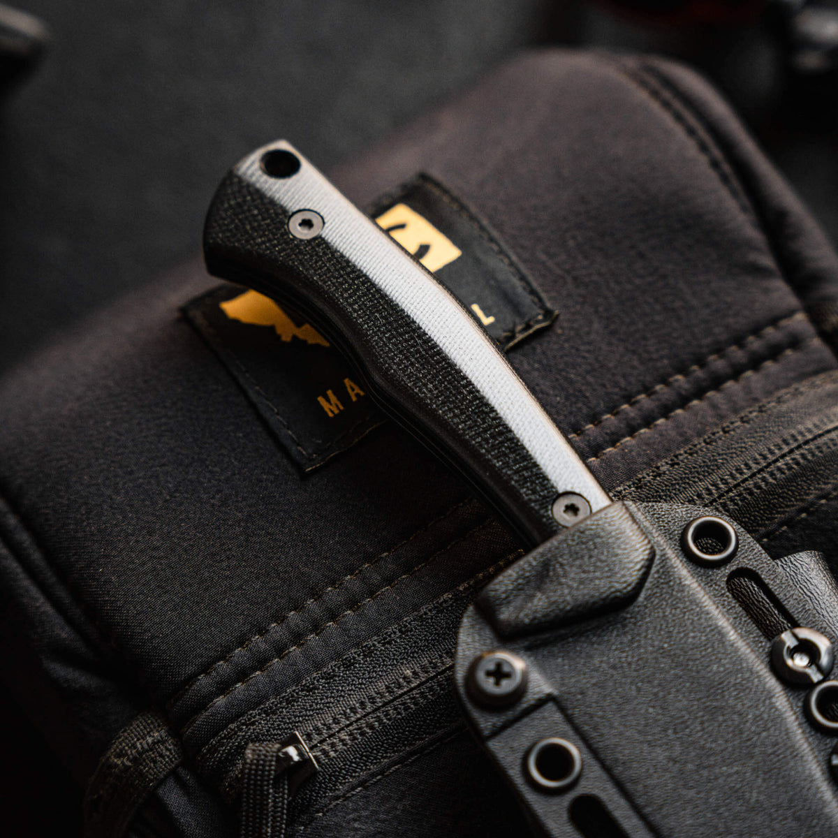 Close-up of the Triumph Pro Black knife handle resting on a tactical bag, showcasing its durable design and grip.