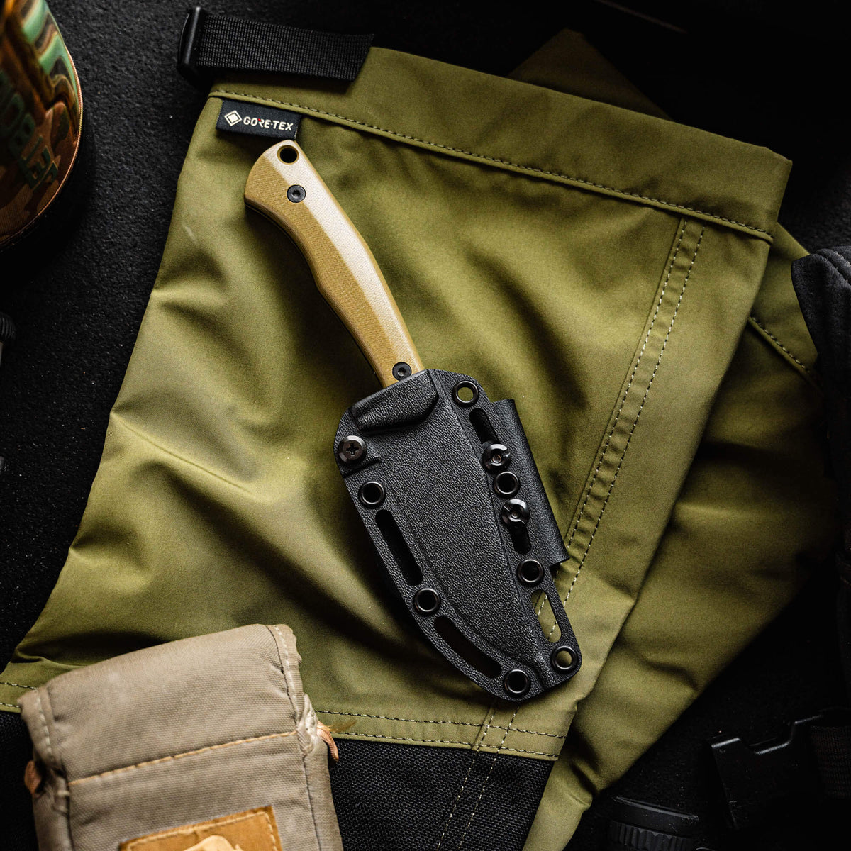 Olive green TRIUMPH PRO knife with a black sheath resting on a textured fabric background, showcasing its rugged design.