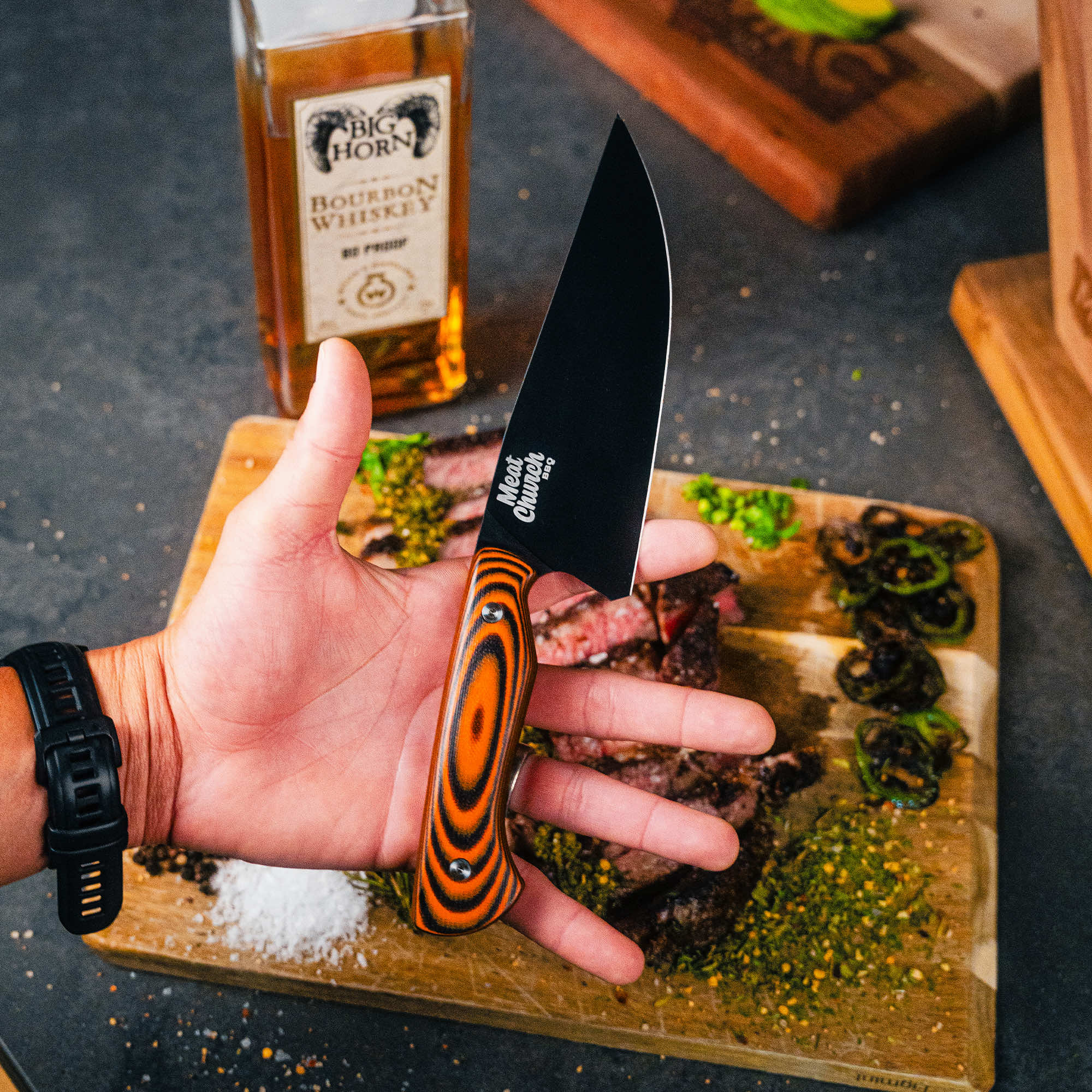 Meat Church chef knife with a striking handle, held above a cutting board with sliced steak and seasonings.