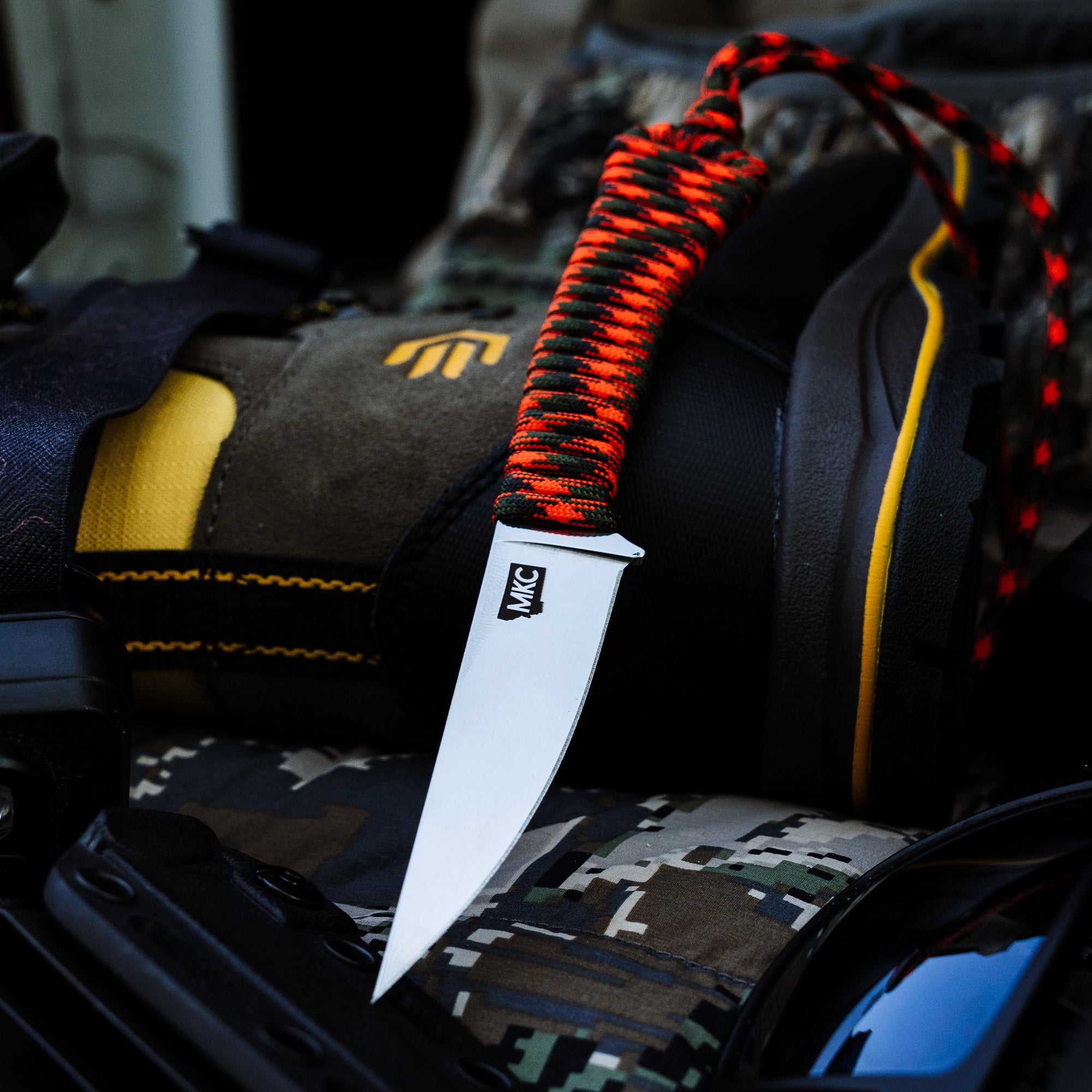 ONX HUNT Mini-Speedgoat 2.0 knife with a bright orange and black paracord handle, resting on outdoor gear.