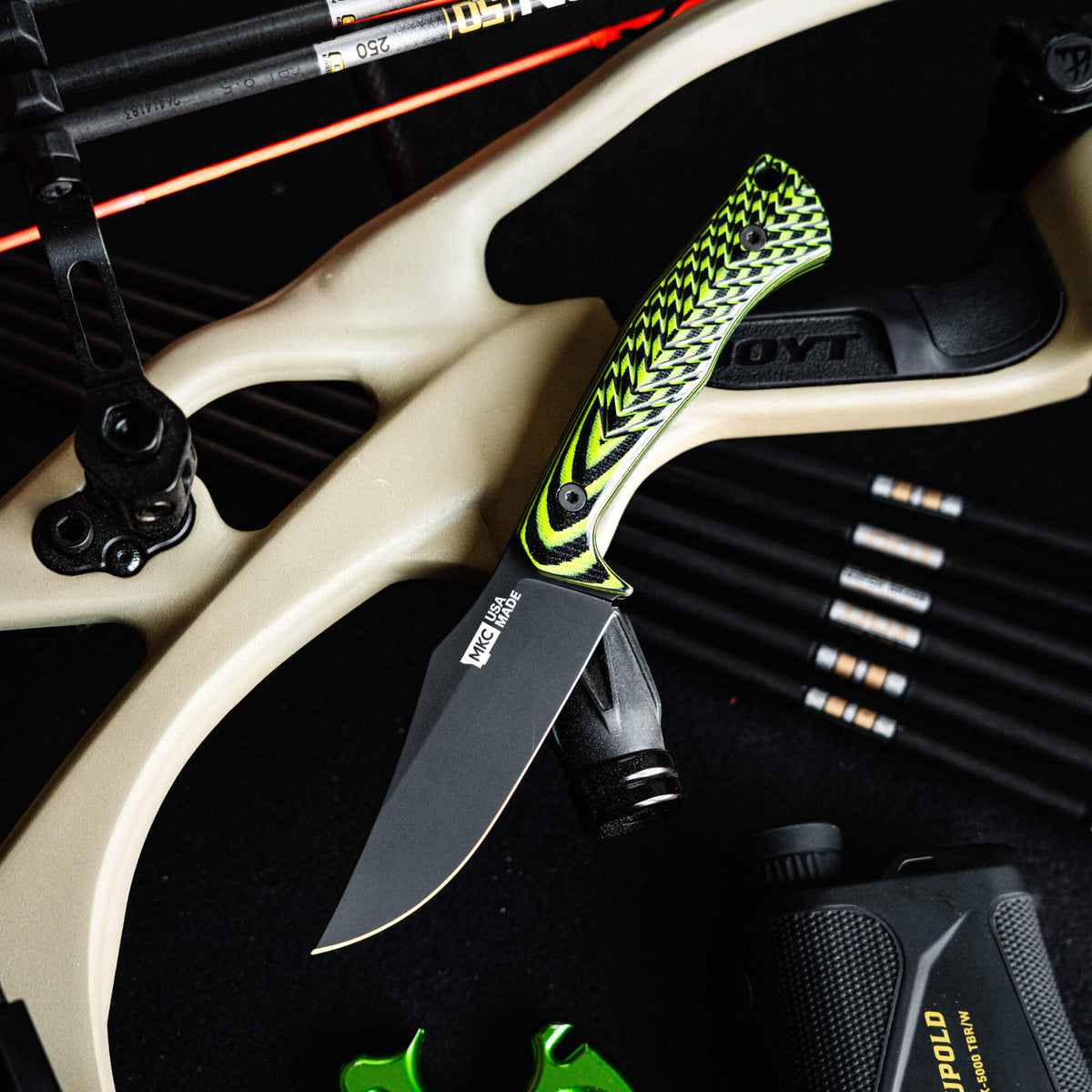 Triumph Pro knife with neon green and black handle, positioned on a bow and surrounded by archery gear.