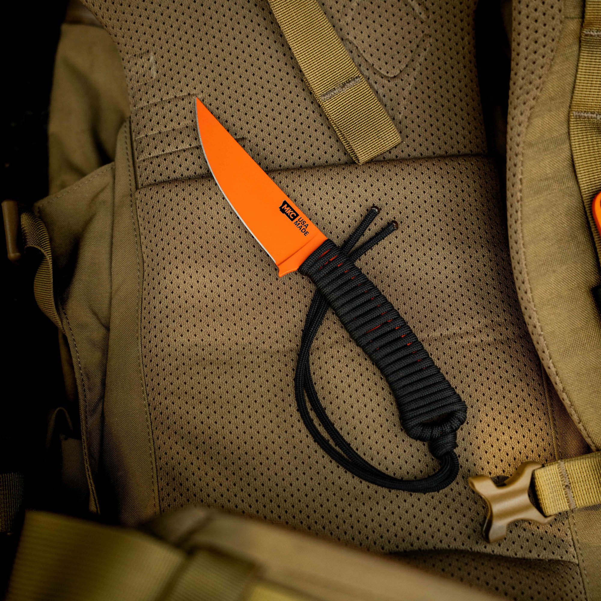 SPEEDGOAT 2.0 knife with blaze orange Cerakote finish resting on a tactical backpack, showcasing its durable design.