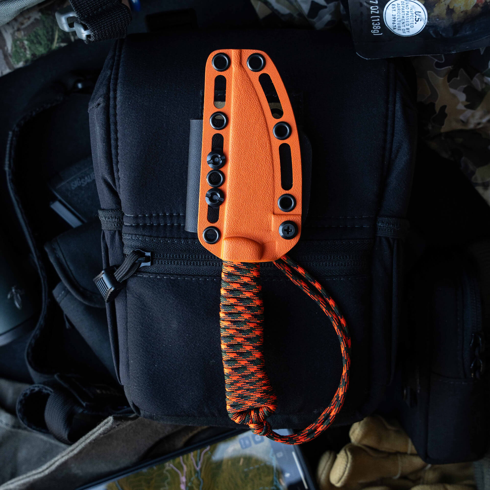 ONX Hunt Magnacut Speedgoat 2.0 knife in orange sheath with paracord handle, resting on a black bag among outdoor gear.