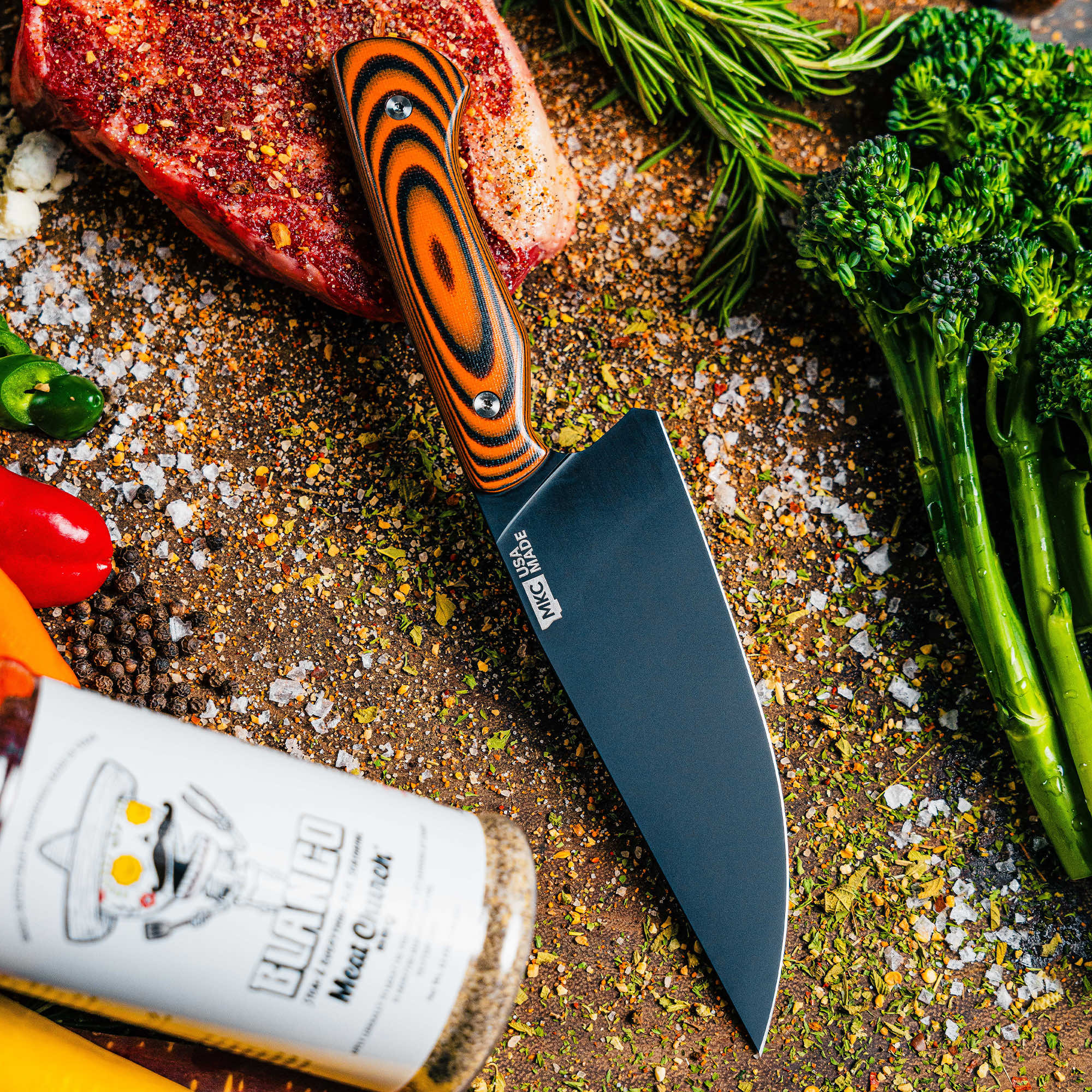 Meat Church chef knife with a sleek black blade and vibrant handle, surrounded by fresh vegetables and spices.