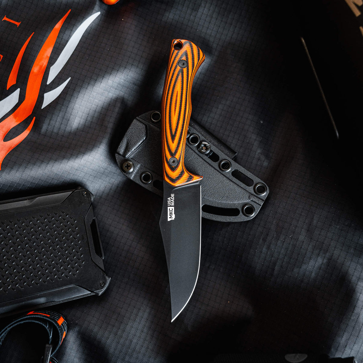 Triumph Pro knife with an orange and black handle, featuring a sleek black blade, displayed on a textured surface.