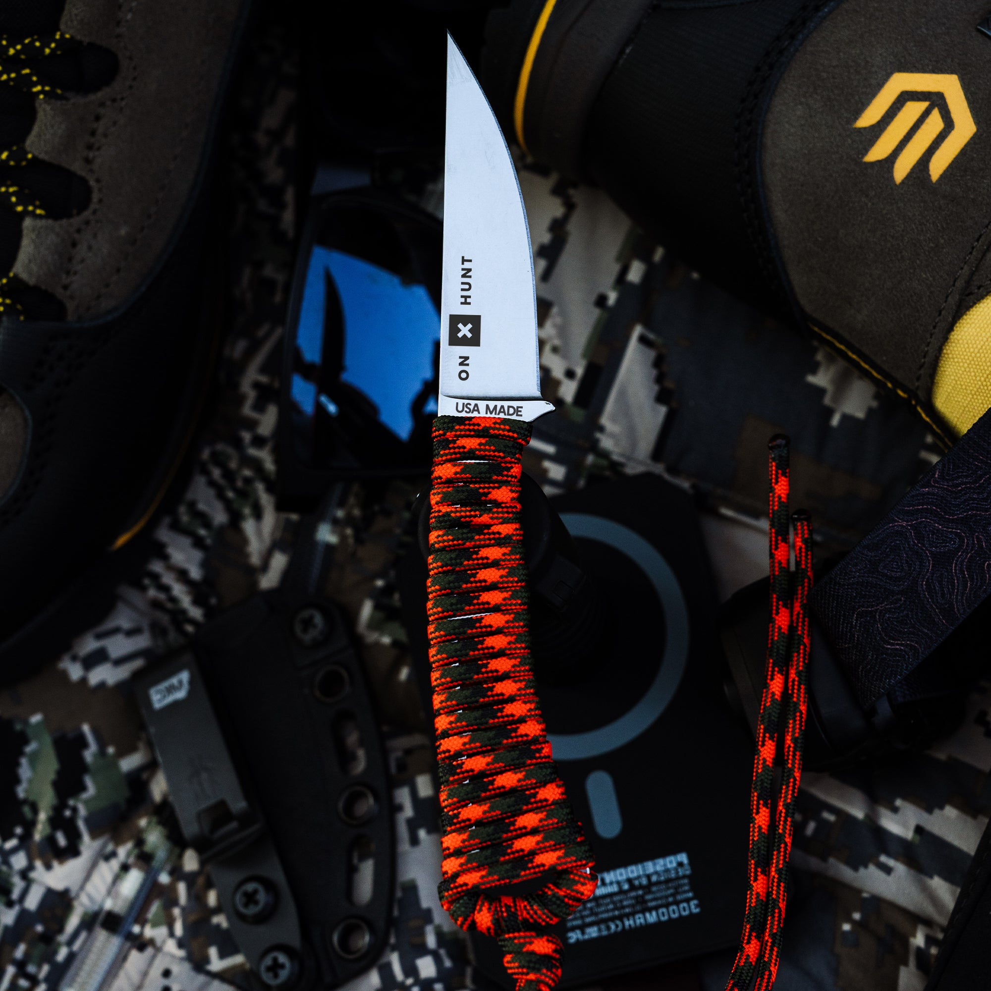 ONX Hunt Mini-Speedgoat 2.0 knife with a red and black paracord handle, surrounded by outdoor gear and tools.