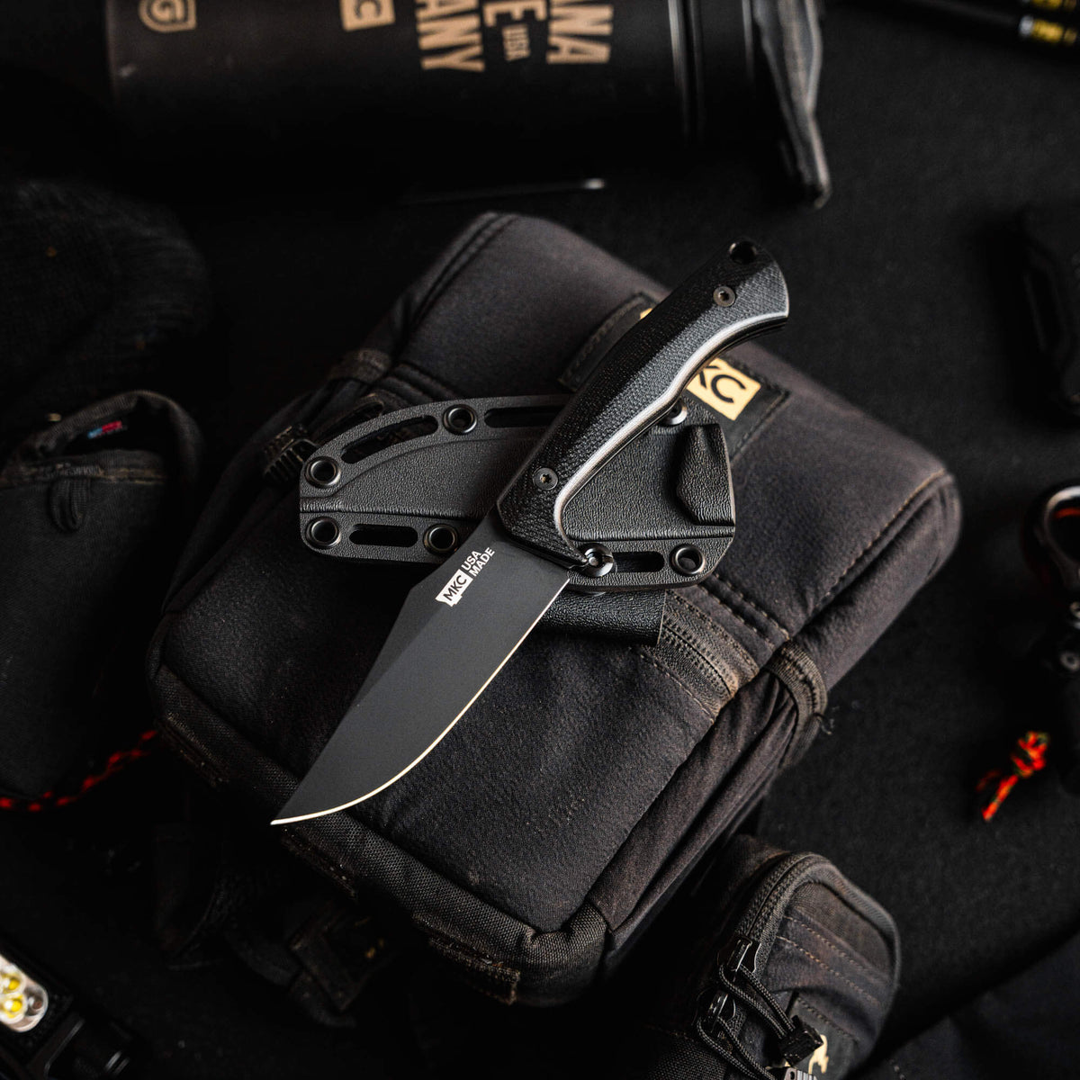 Triumph Pro Black knife with a sleek black blade and textured handle, resting on a tactical bag and gear.