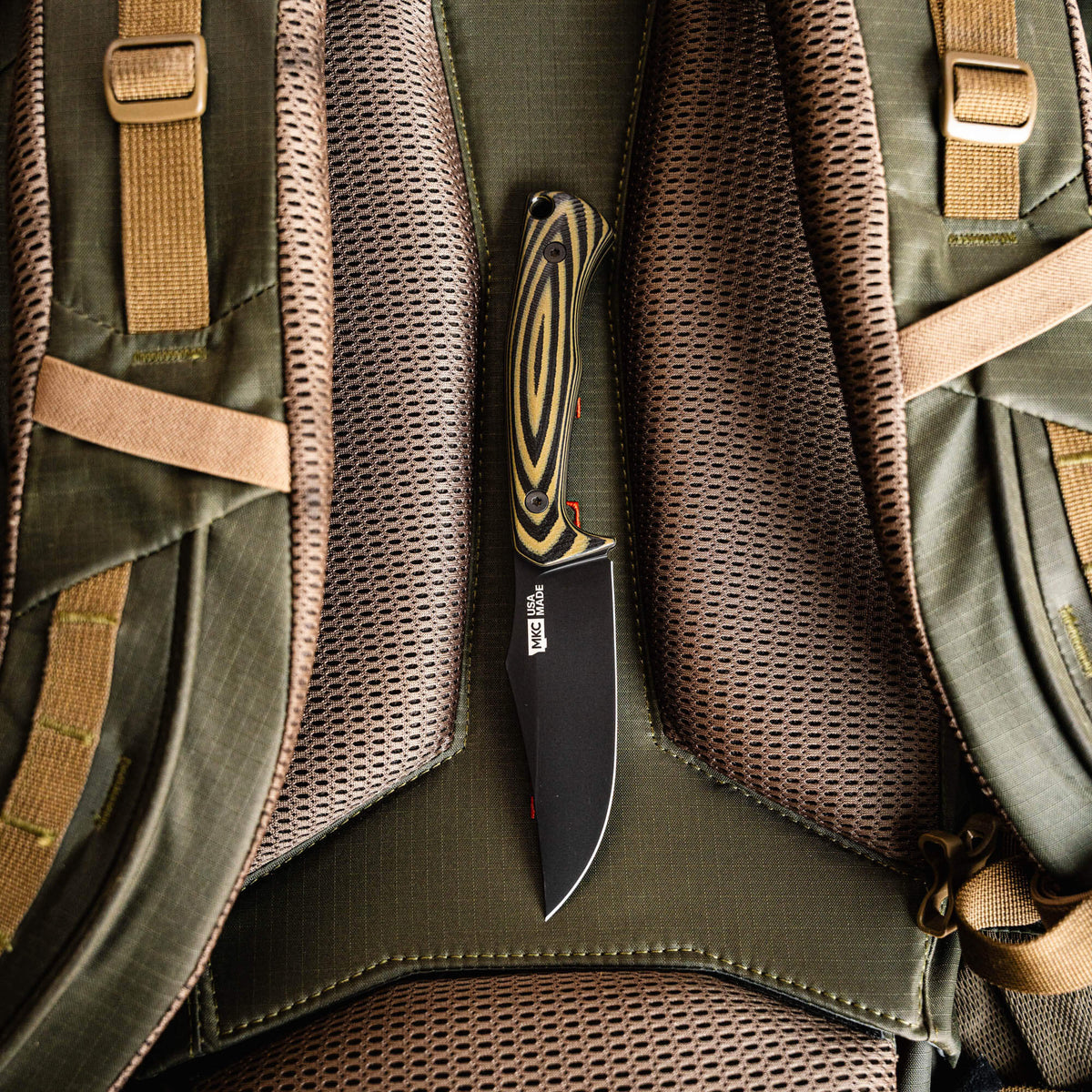 Triumph Pro knife in green and black resting on a textured backpack, showcasing its sleek design and durable blade.