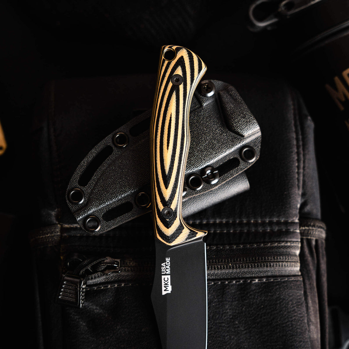 Triumph Pro knife with tan and black handle, featuring a sleek blade and protective sheath, resting on a textured surface.