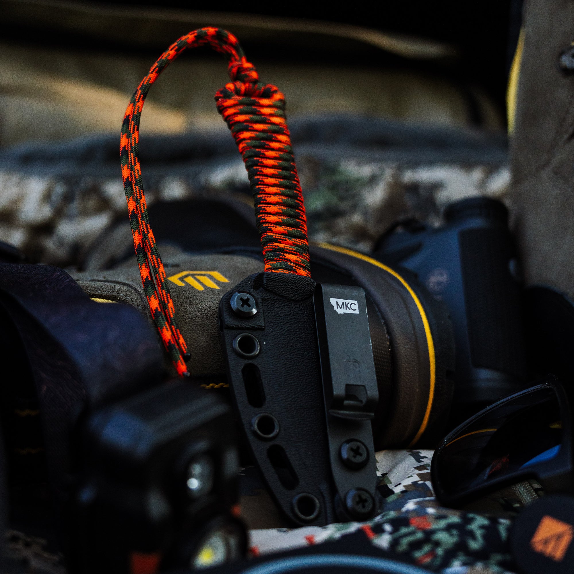 ONX Hunt Mini-Speedgoat 2.0 knife with a vibrant paracord lanyard, resting among outdoor gear and equipment.