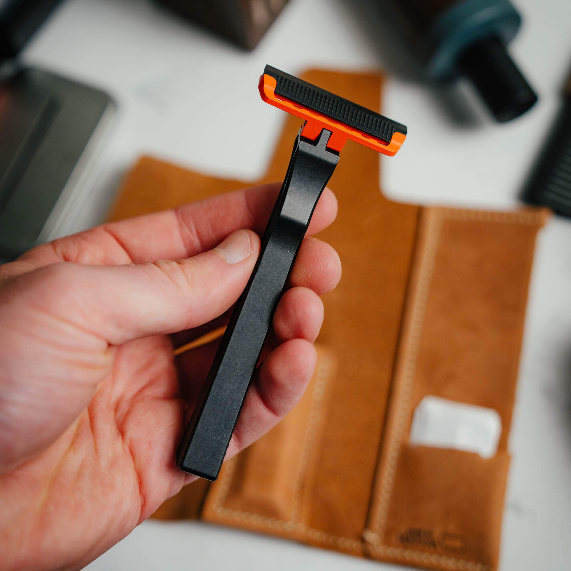 EDC Razor 2.0 by Montana Knife Company, featuring a sleek black handle and vibrant orange accents, held in hand.